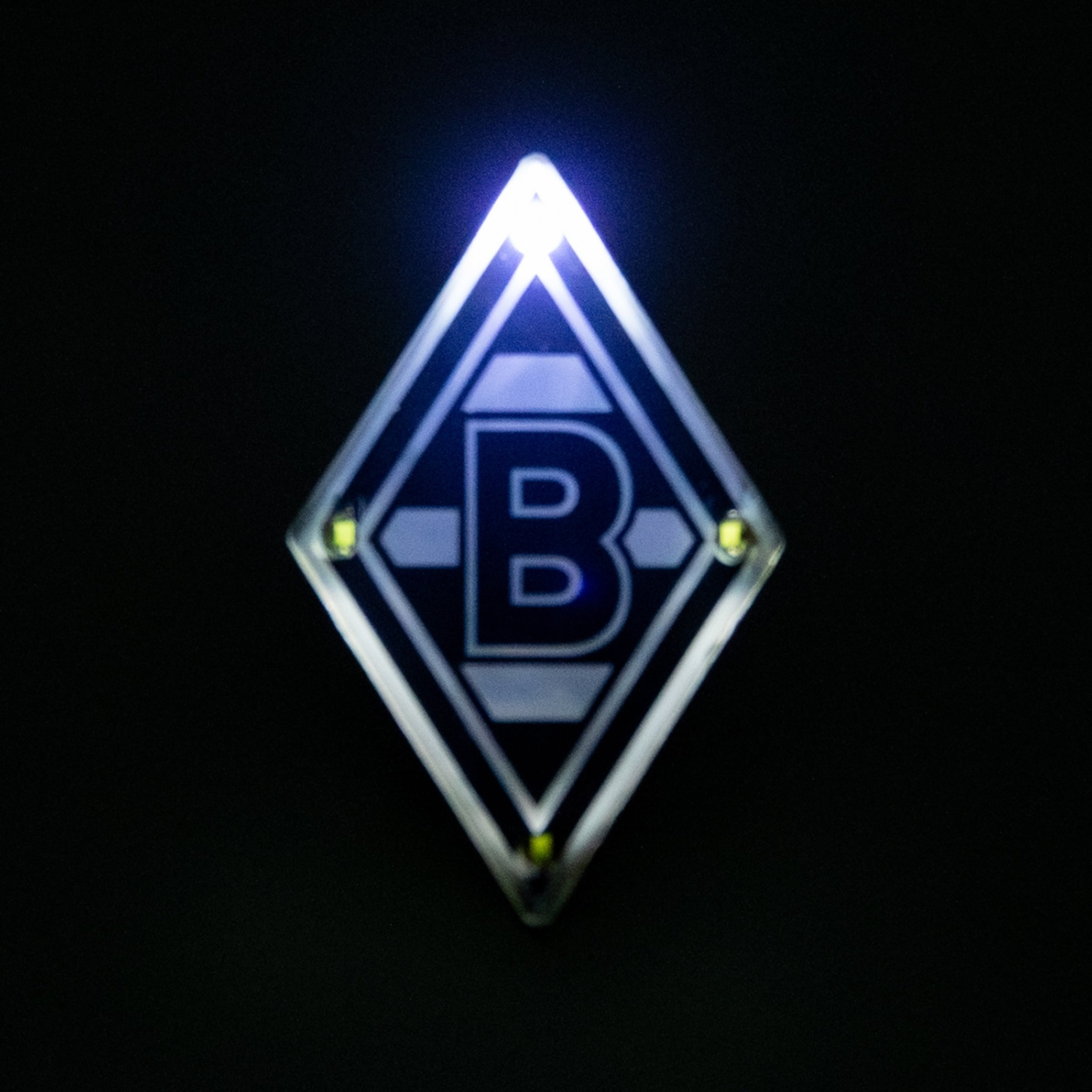 Beleuchtetes Logo von Borussia Mönchengladbach: Eine weiße Raute mit schwarzem B auf dunklem Hintergrund.