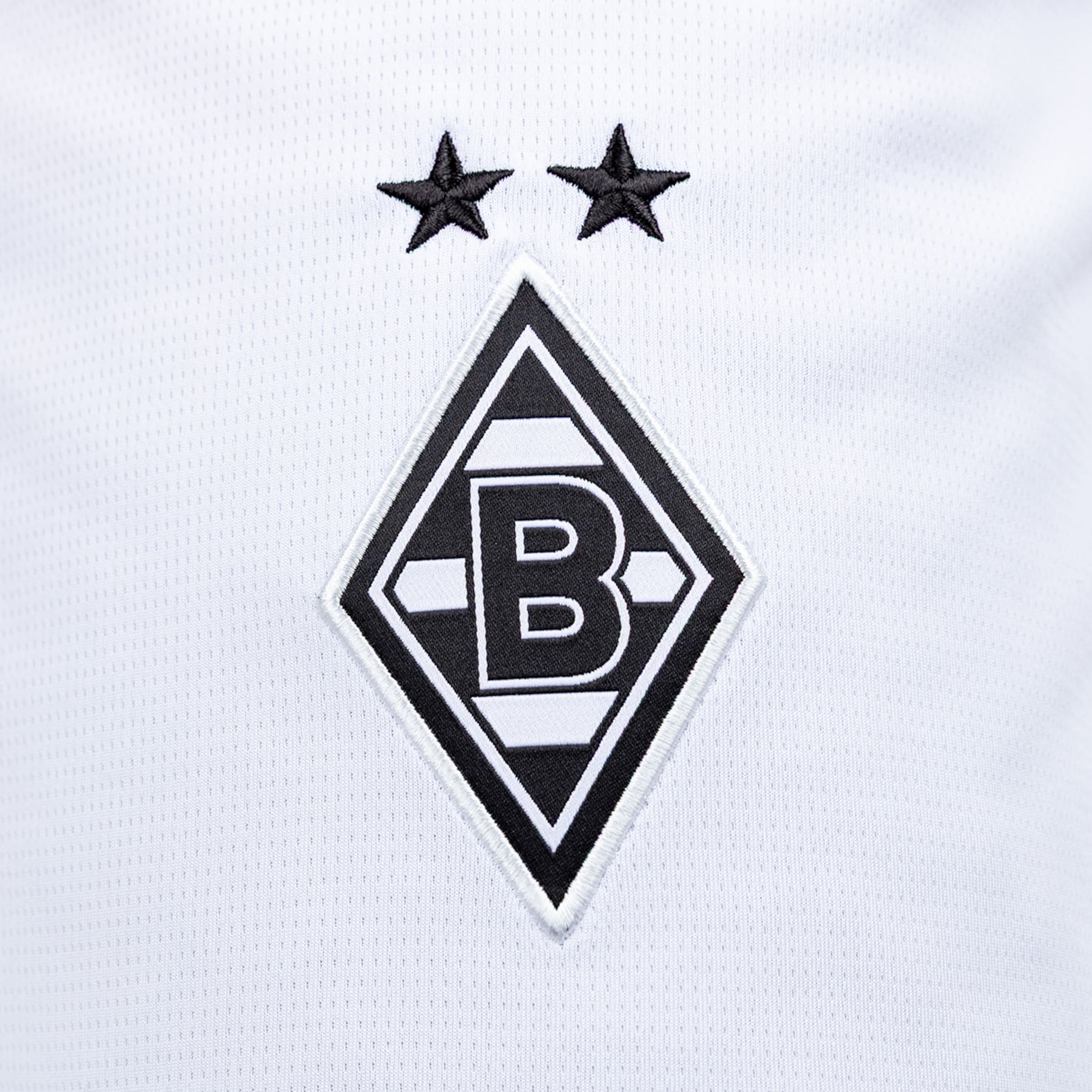 Stickerei des Borussia Mönchengladbach Logos auf weißem Stoff: schwarz-weißes Rauten-Wappen mit dem Buchstaben B und zwei Sternen darüber.