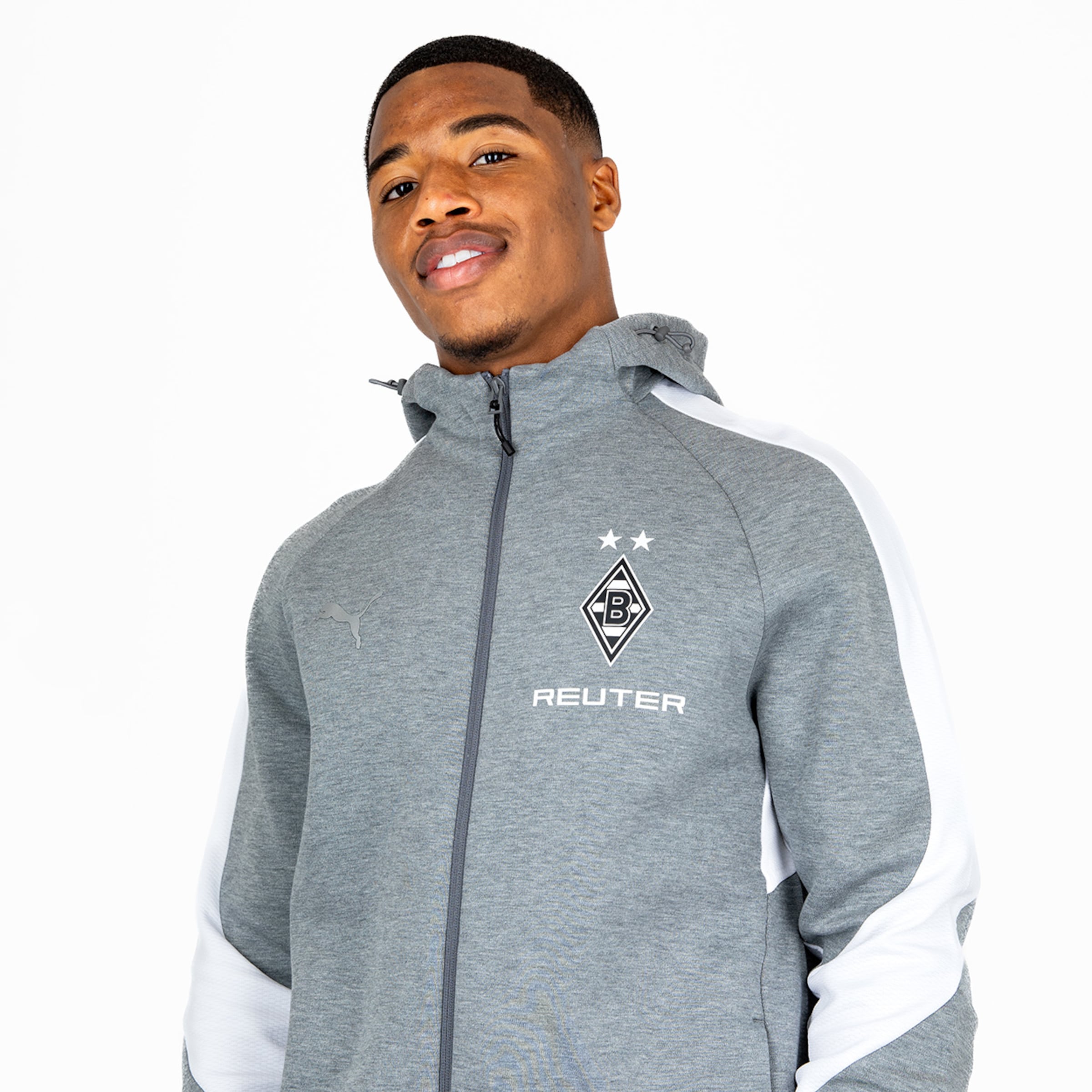 Ein Spieler von Borussia Mönchengladbach trägt eine graue Sportjacke mit Logo und lächelt in die Kamera.