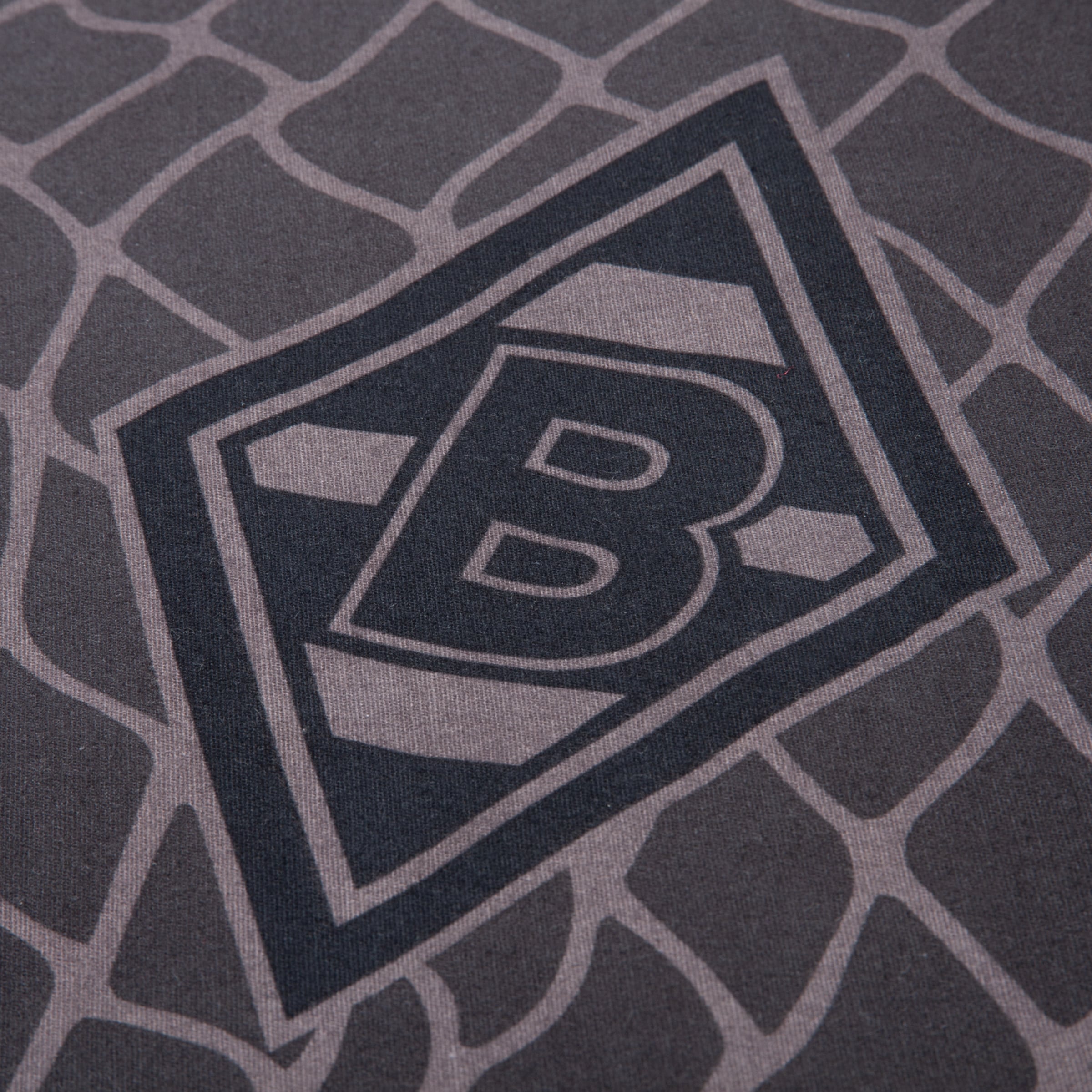Nahaufnahme eines schwarzen Rauten-Logos mit dem Buchstaben B auf grauem Stoff mit einem Muster in Giraffen-Optik.