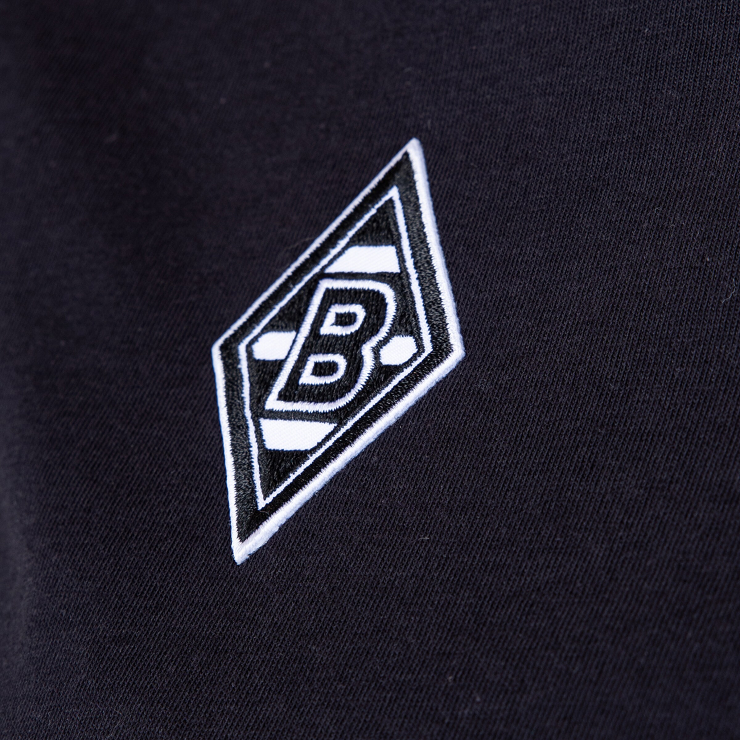 Nahaufnahme des aufgestickten Borussia Mönchengladbach-Logos in Rautenform auf schwarzem Stoff.