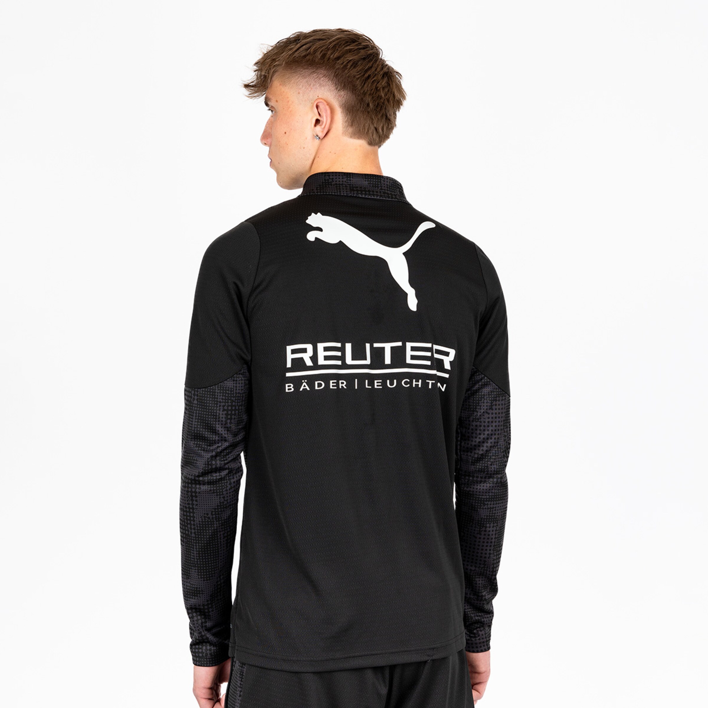 Junger Mann in einem schwarzen Sportoberteil mit Puma-Logo und Sponsorenaufdruck.
