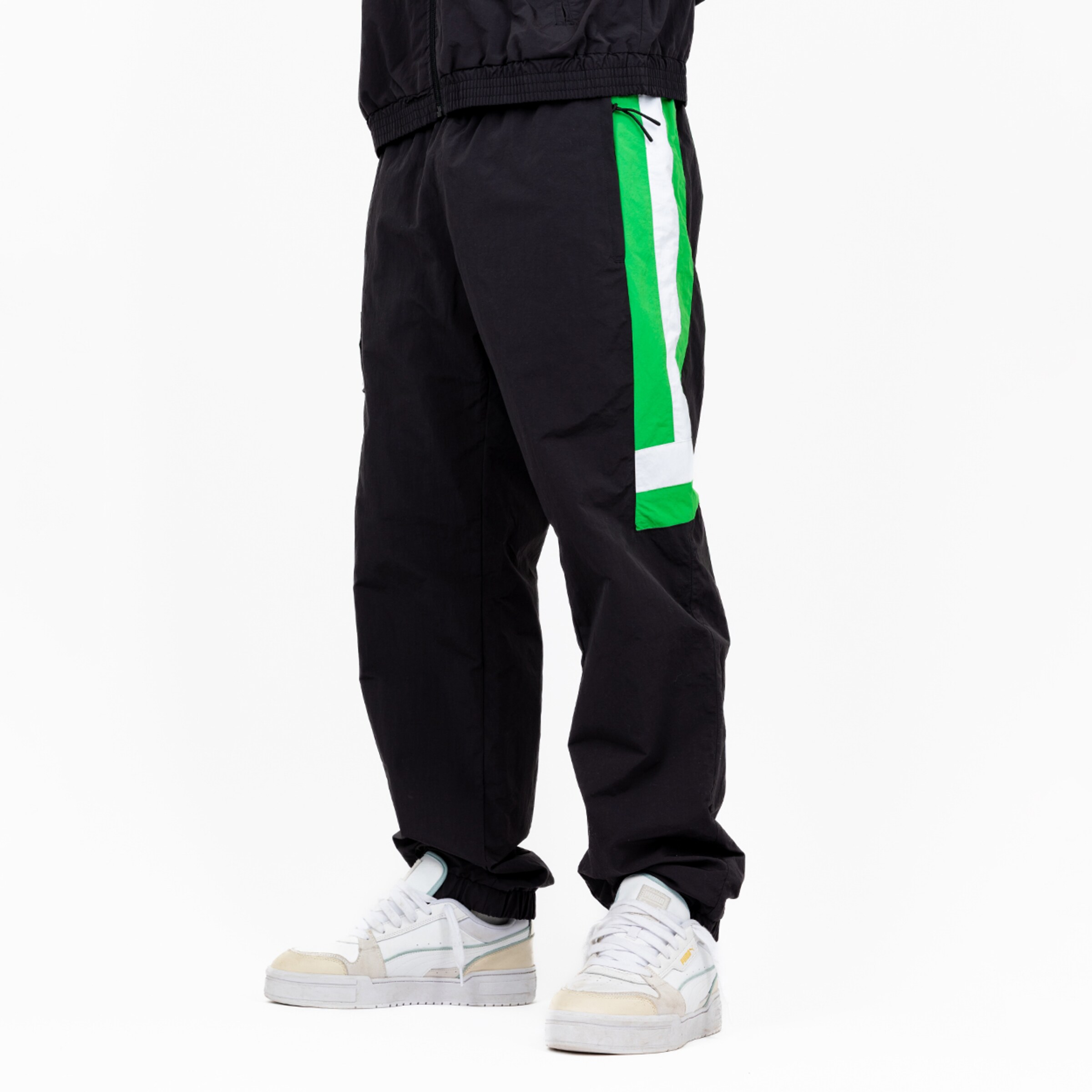 Schwarze Sporthose mit grünen Streifen kombiniert mit weißen Sneakers.