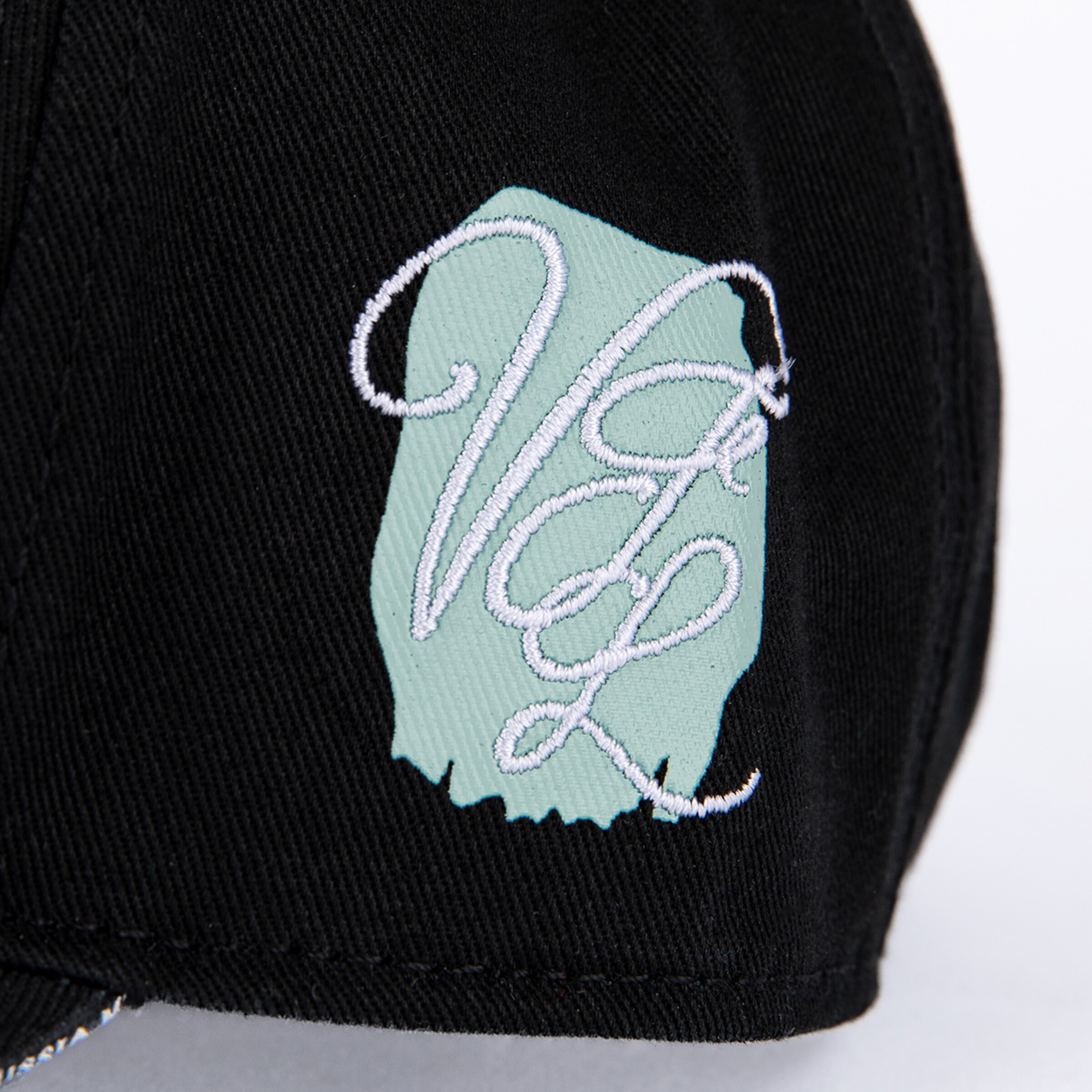 Nahaufnahme einer weißen VGL-Stickerei in Schreibschrift auf einem mintgrünen Untergrund, auf schwarzem Twill-Stoff.