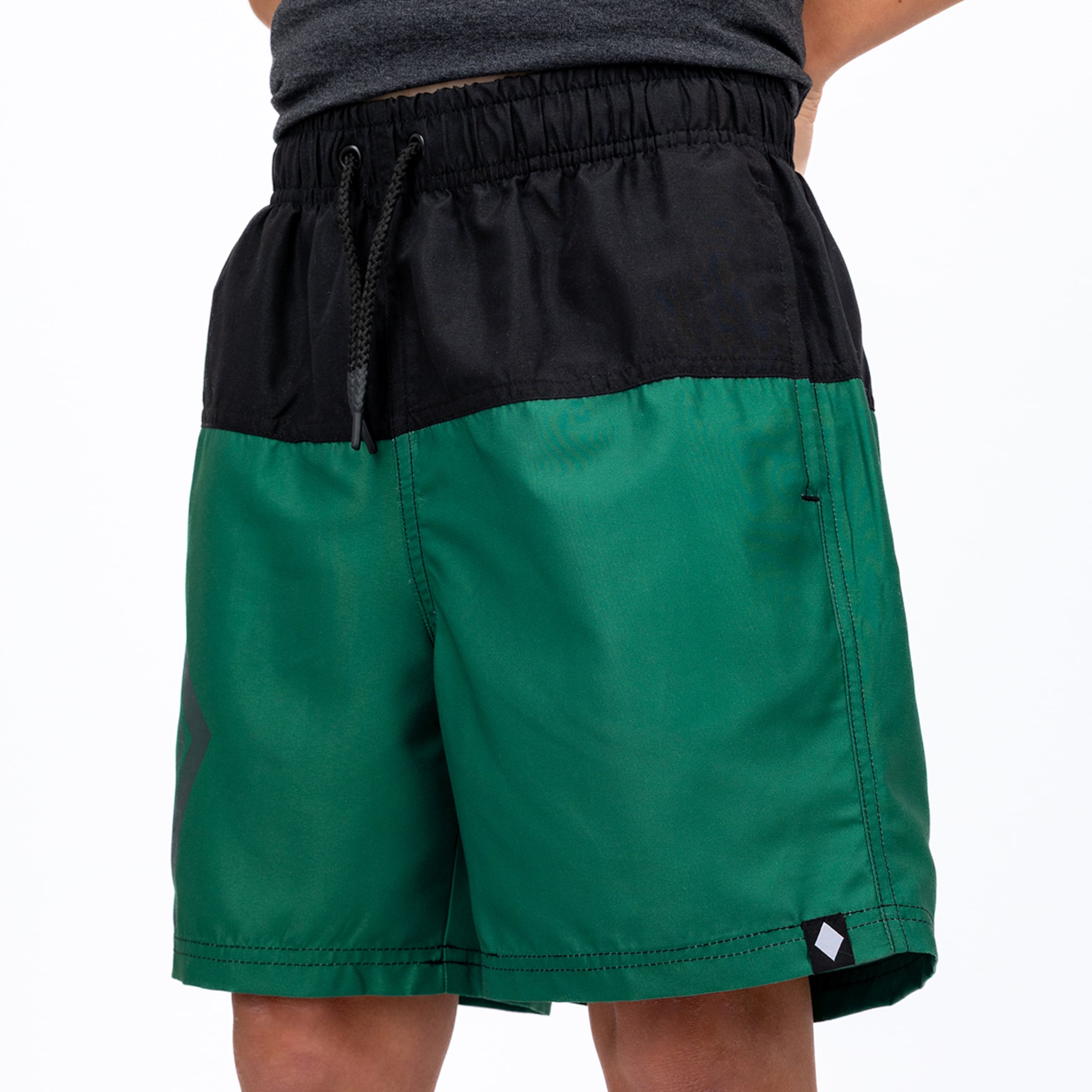 Close-up of a person wearing black and green color-block athletic shorts with a drawstring waist. The shorts feature a subtle logo on the left leg and a white diamond logo tag on the right hem.