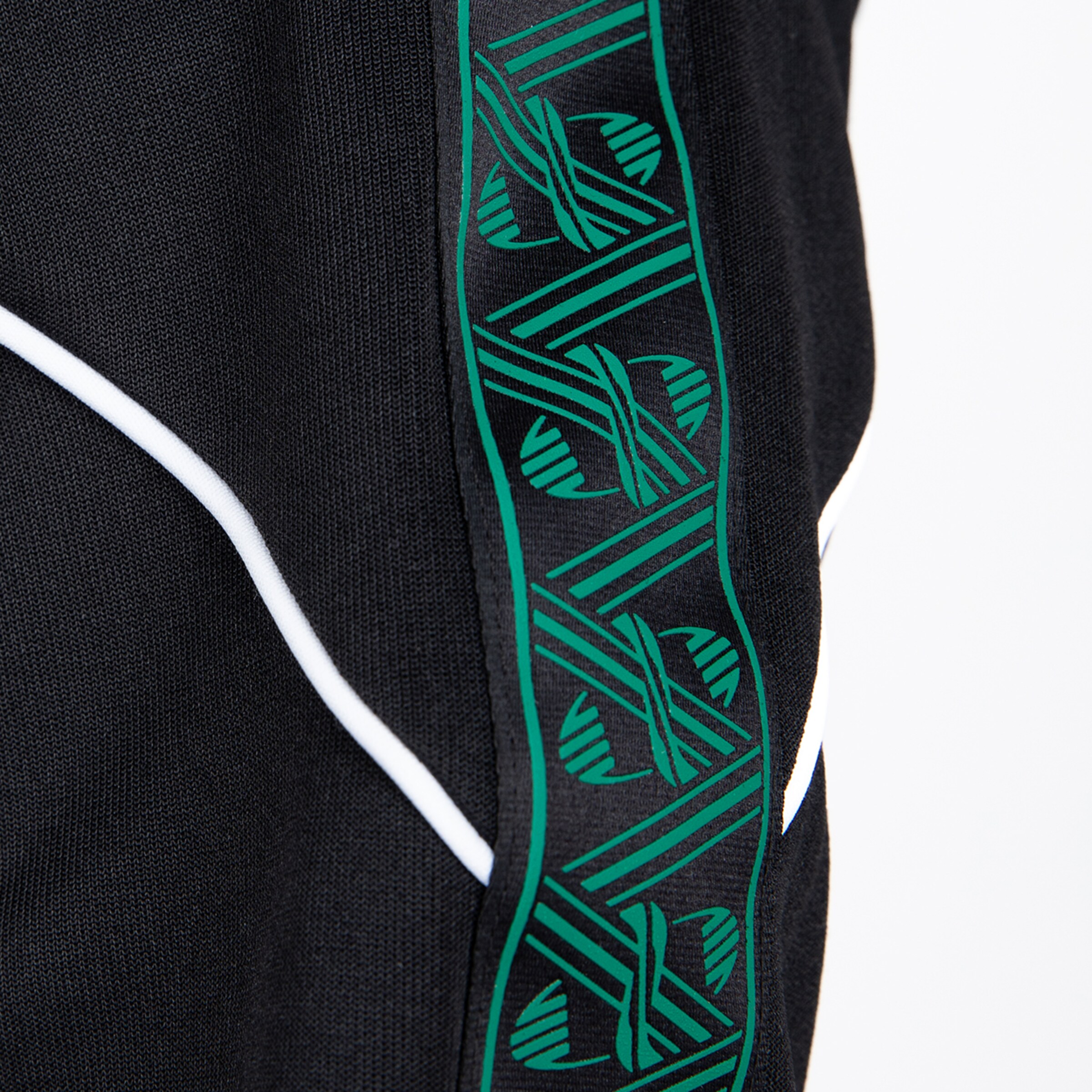 Nahaufnahme schwarzer Sportkleidung mit weißer Paspelierung und einem grünen Zierstreifen mit geometrischem Muster.