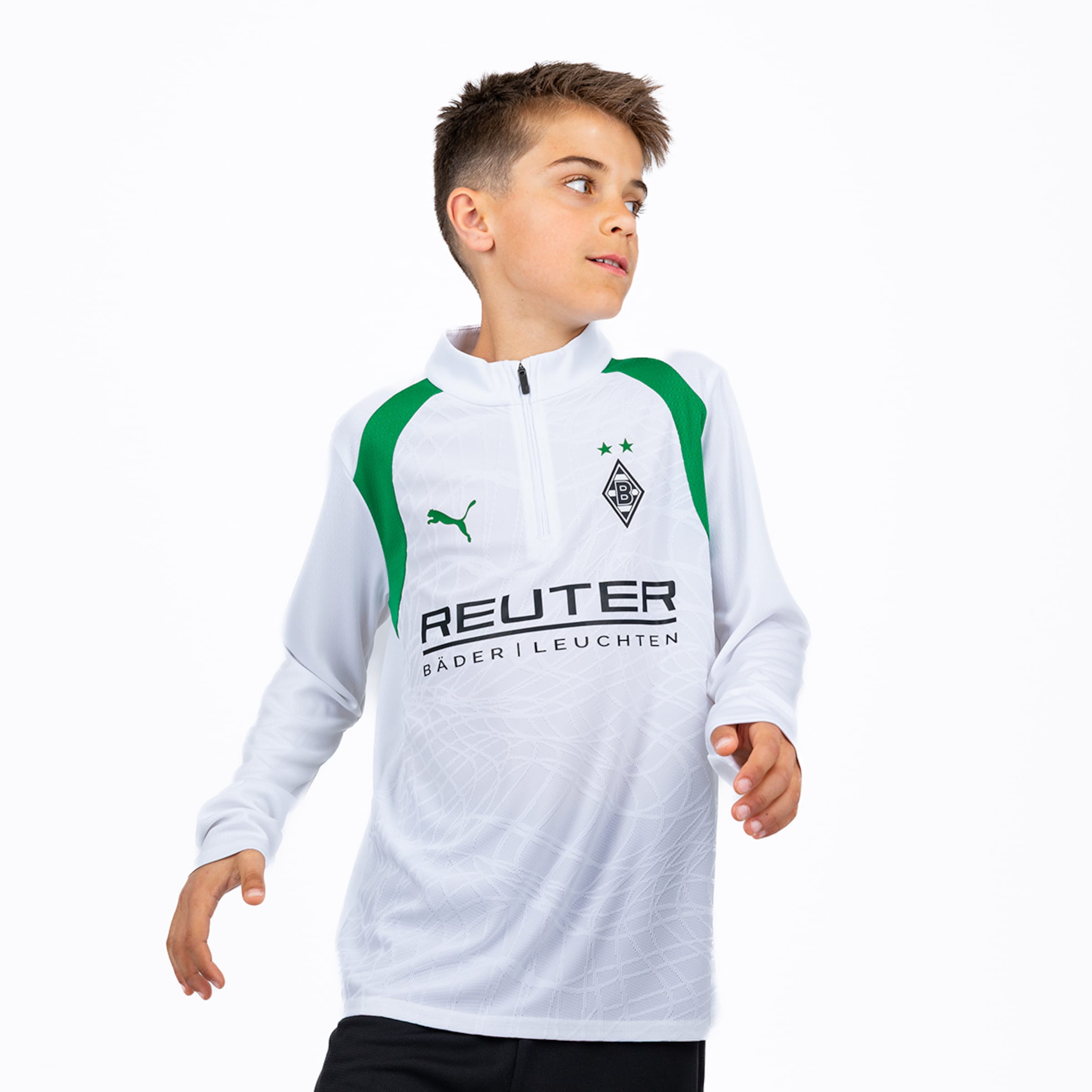 Ein junger Junge in einem weiß-grünen, langärmeligen Borussia Mönchengladbach Fußball-Trainingsoberteil von Puma mit Sponsor Reuter blickt nach rechts.