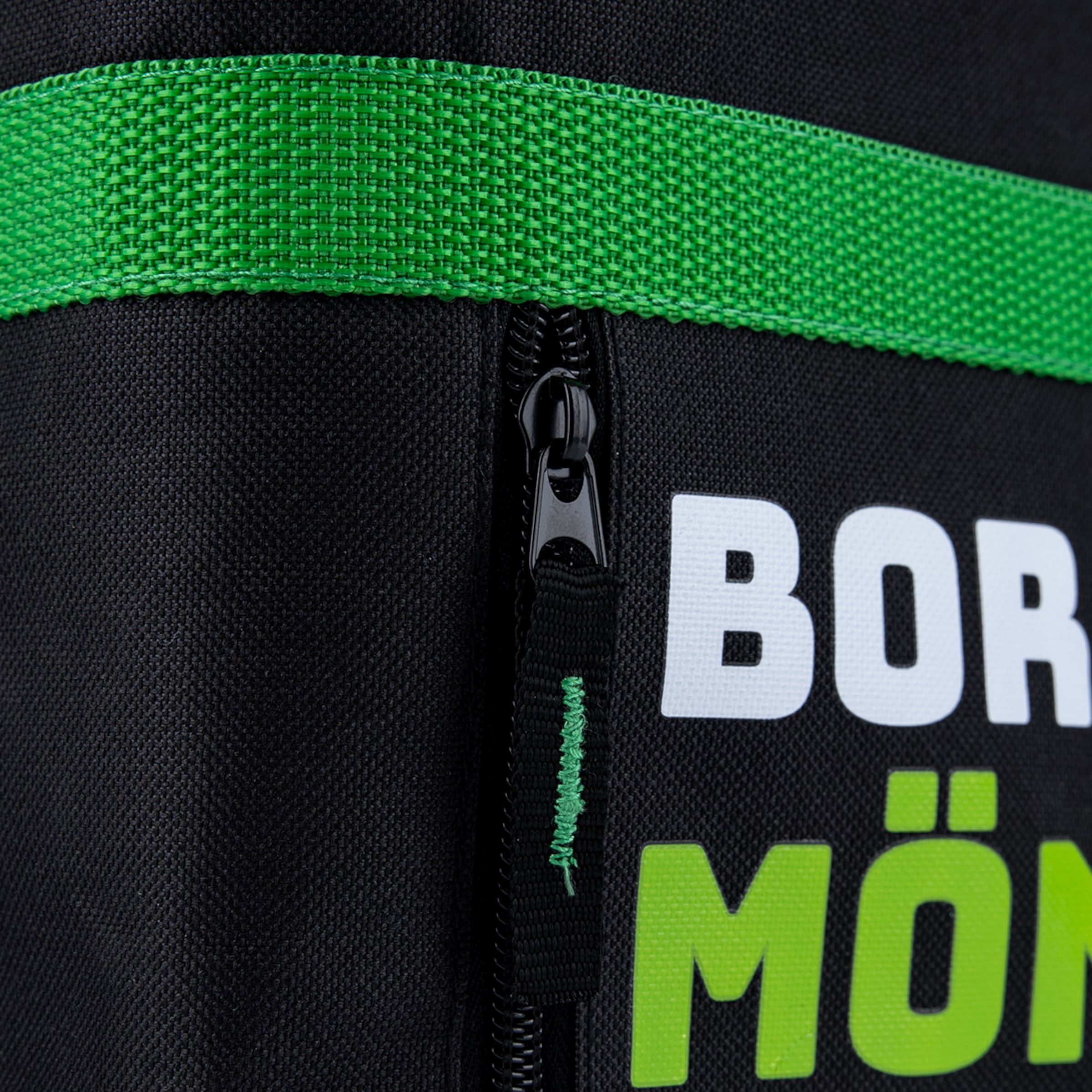 Nahaufnahme einer schwarzen Tasche mit grünem Band, Reißverschluss und den Buchstaben „BOR“ in Weiß sowie „MÖN“ in Hellgrün.