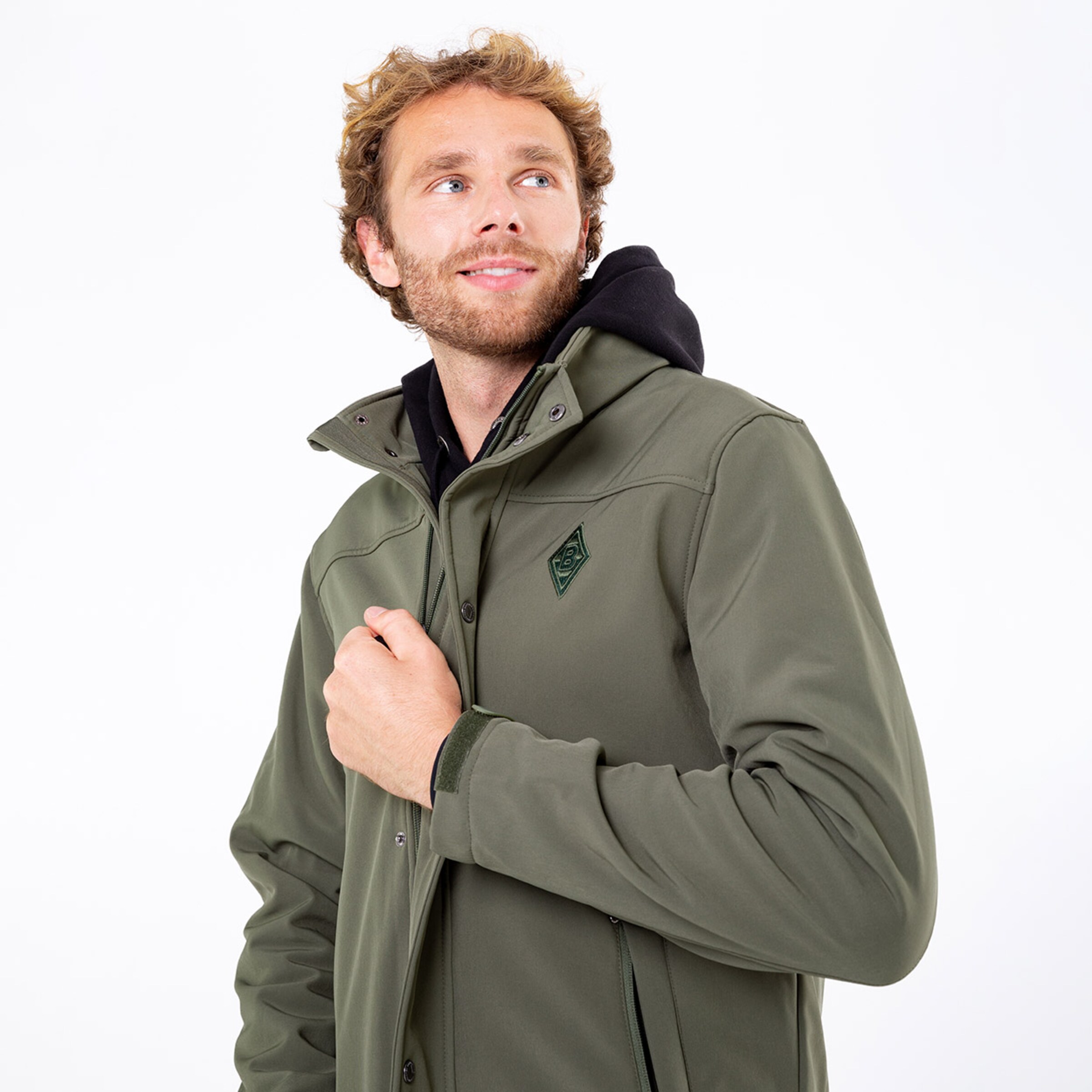 Mann in olivgrüner Jacke mit Kapuze lächelnd und in Richtung rechts schauend.