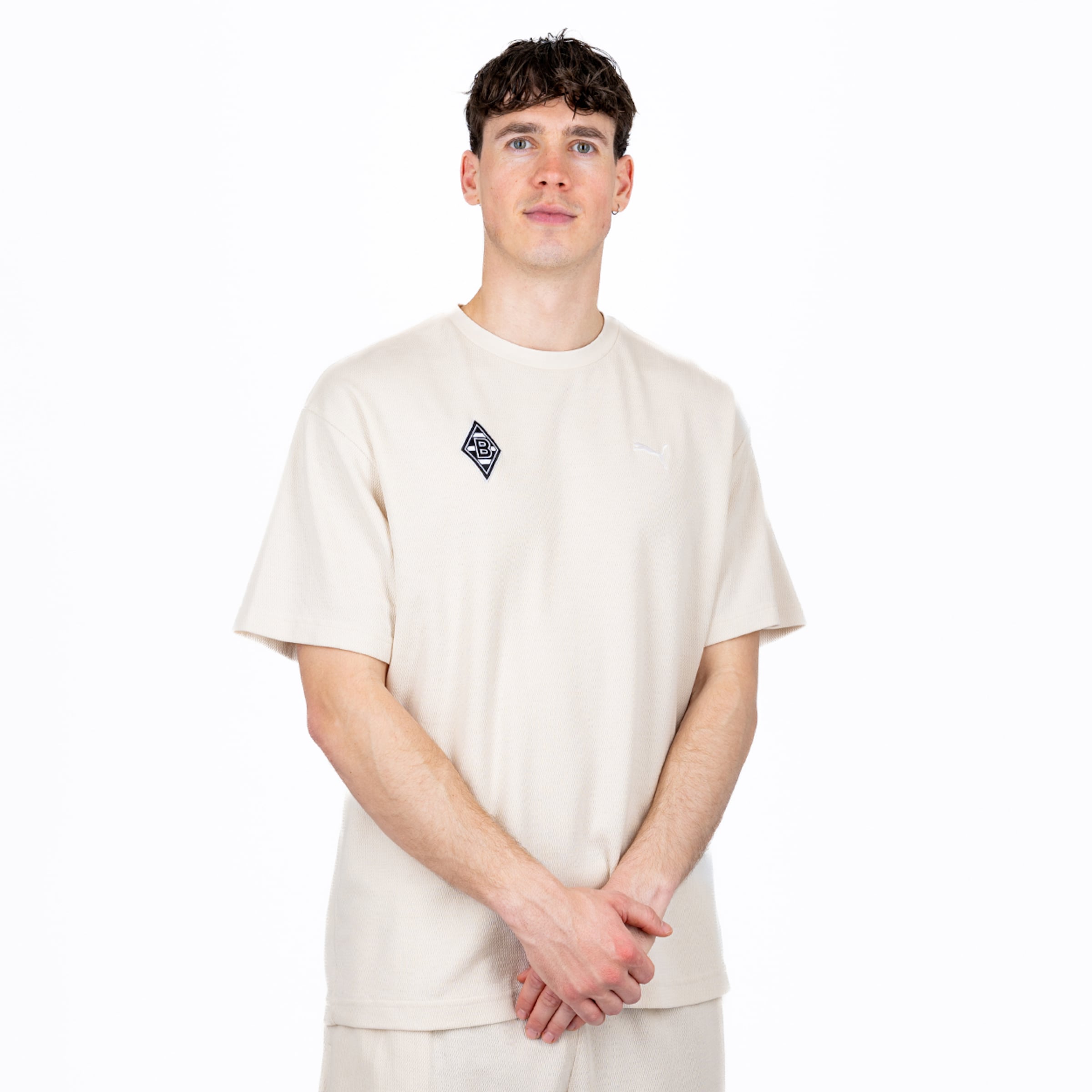 Mann in beigem Borussia Mönchengladbach T-Shirt von Puma vor weißem Hintergrund.