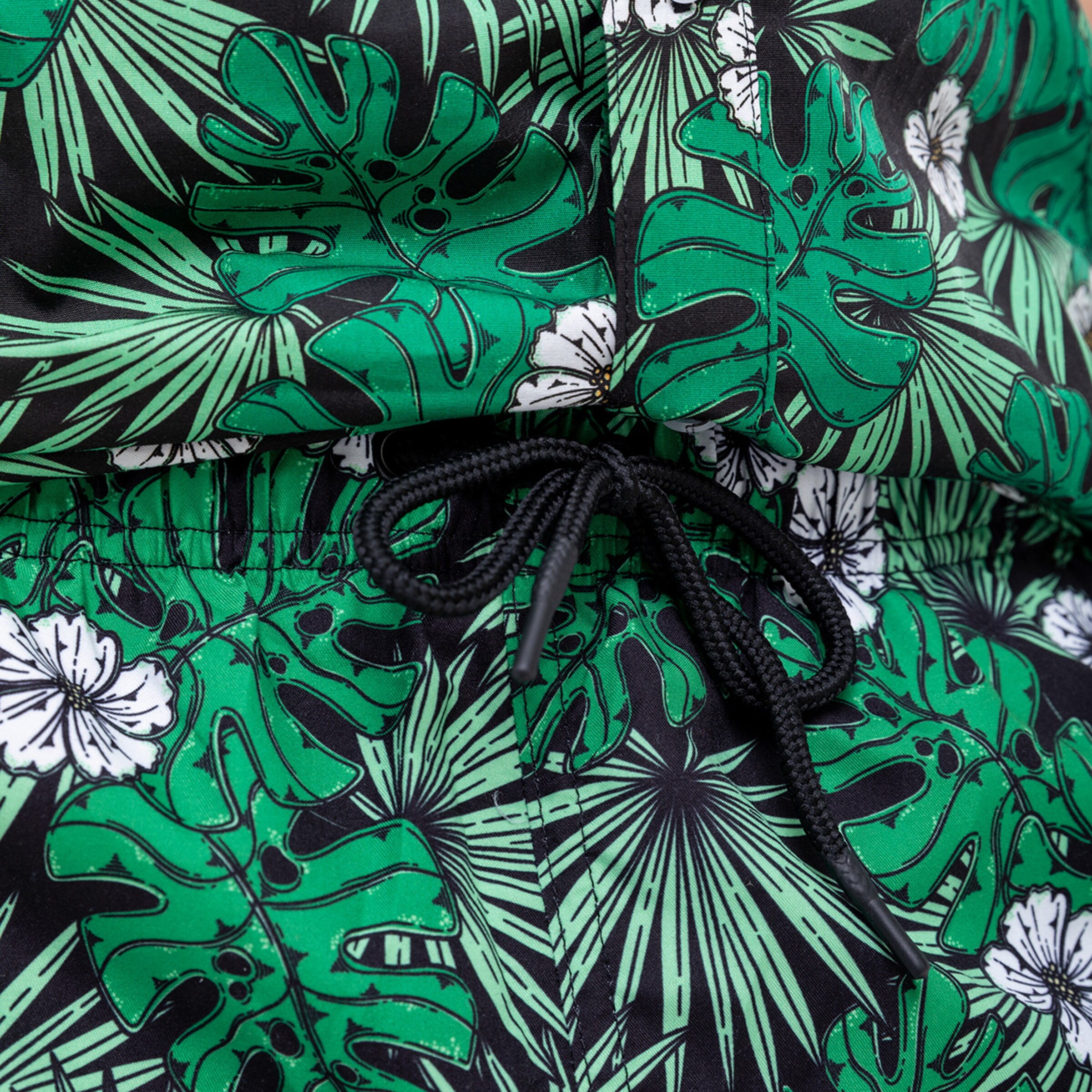 Schwarze Shorts mit grünem Palmenblattmuster und weißen Blumen.