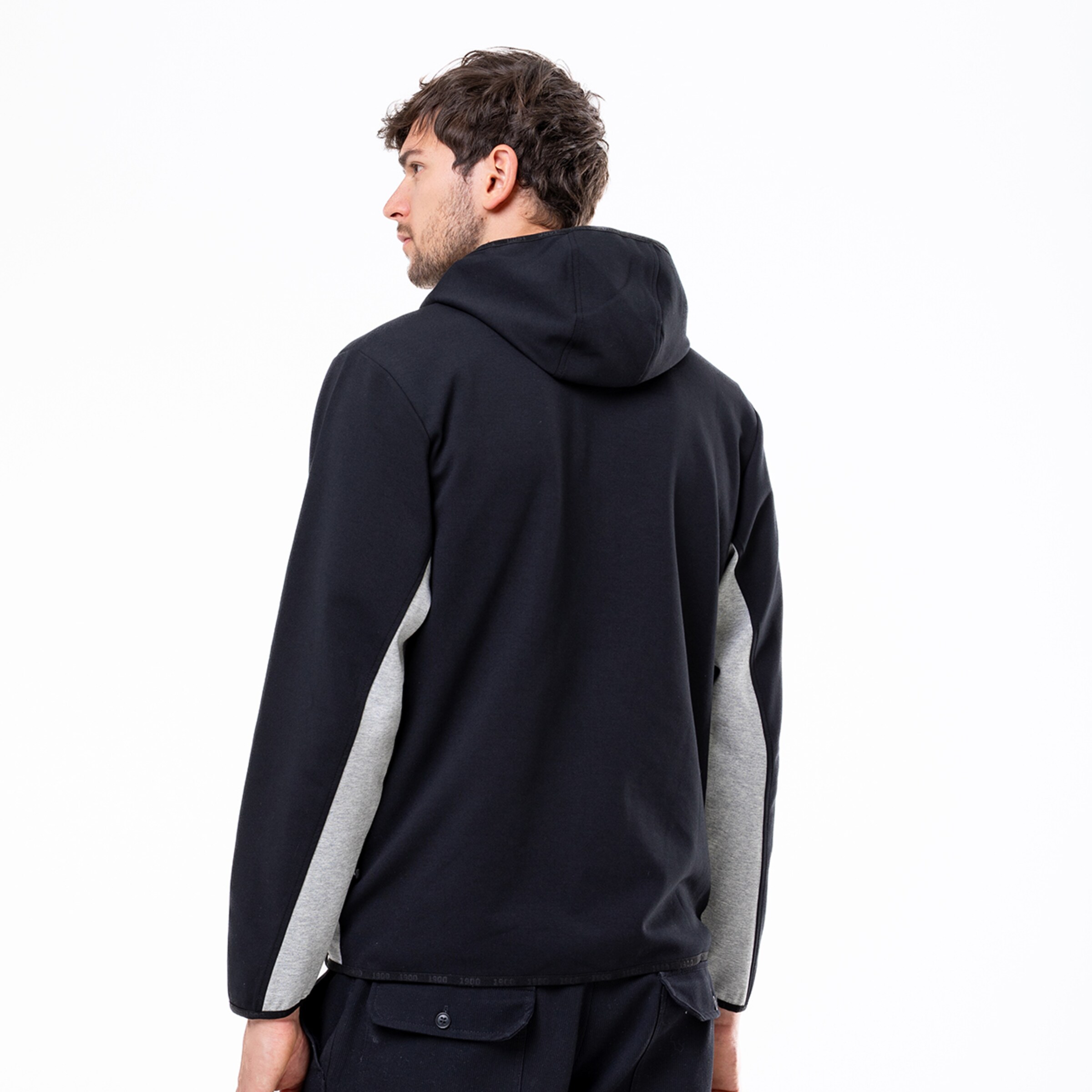 Ein Mann trägt einen Kapuzenpullover mit grau-schwarzen Ärmeln von hinten gesehen.