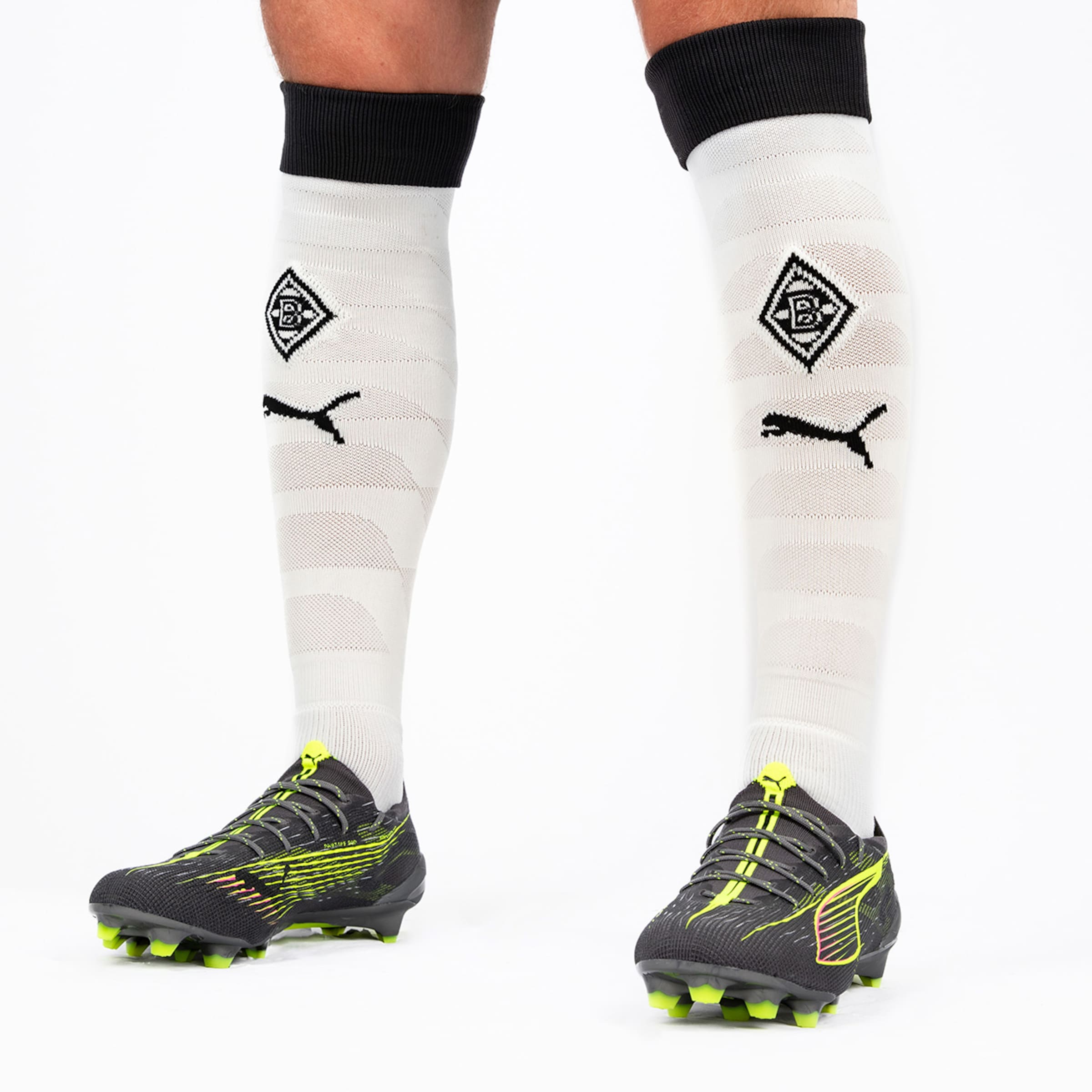 Black soccer shoes with yellow accents and white shin guards featuring Borussia Mönchengladbach logo and Puma symbol.