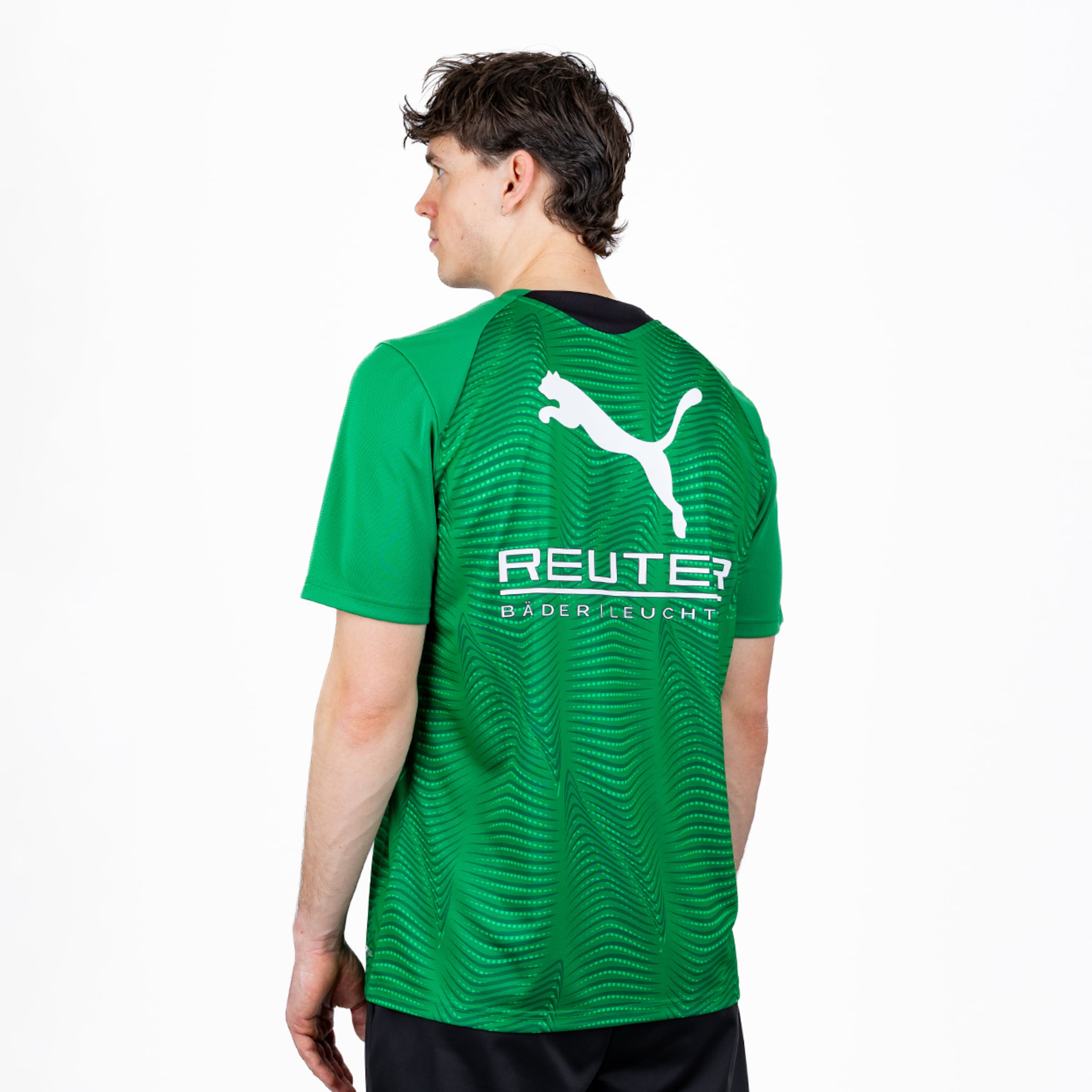 Ein Mann von hinten, leicht gedreht, trägt ein grünes Sportshirt mit weißem Puma-Logo und dem Schriftzug 'REUTER BÄDER LEUCHT' auf dem Rücken. Das Shirt hat ein wellenförmiges Muster.