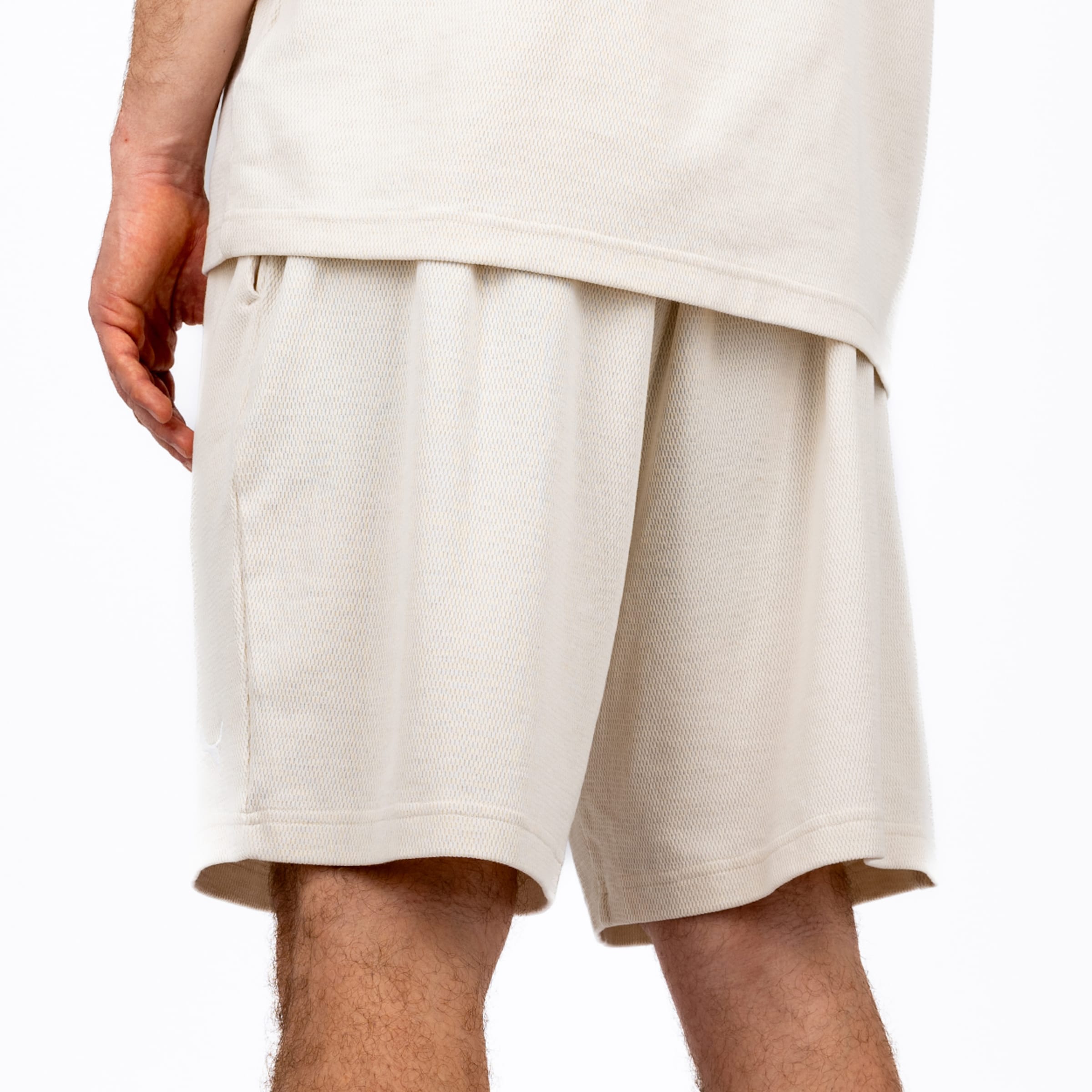 Rückansicht einer Person in hellbeigen Mesh-Shorts und passendem T-Shirt mit Wabenstruktur vor weißem Hintergrund.