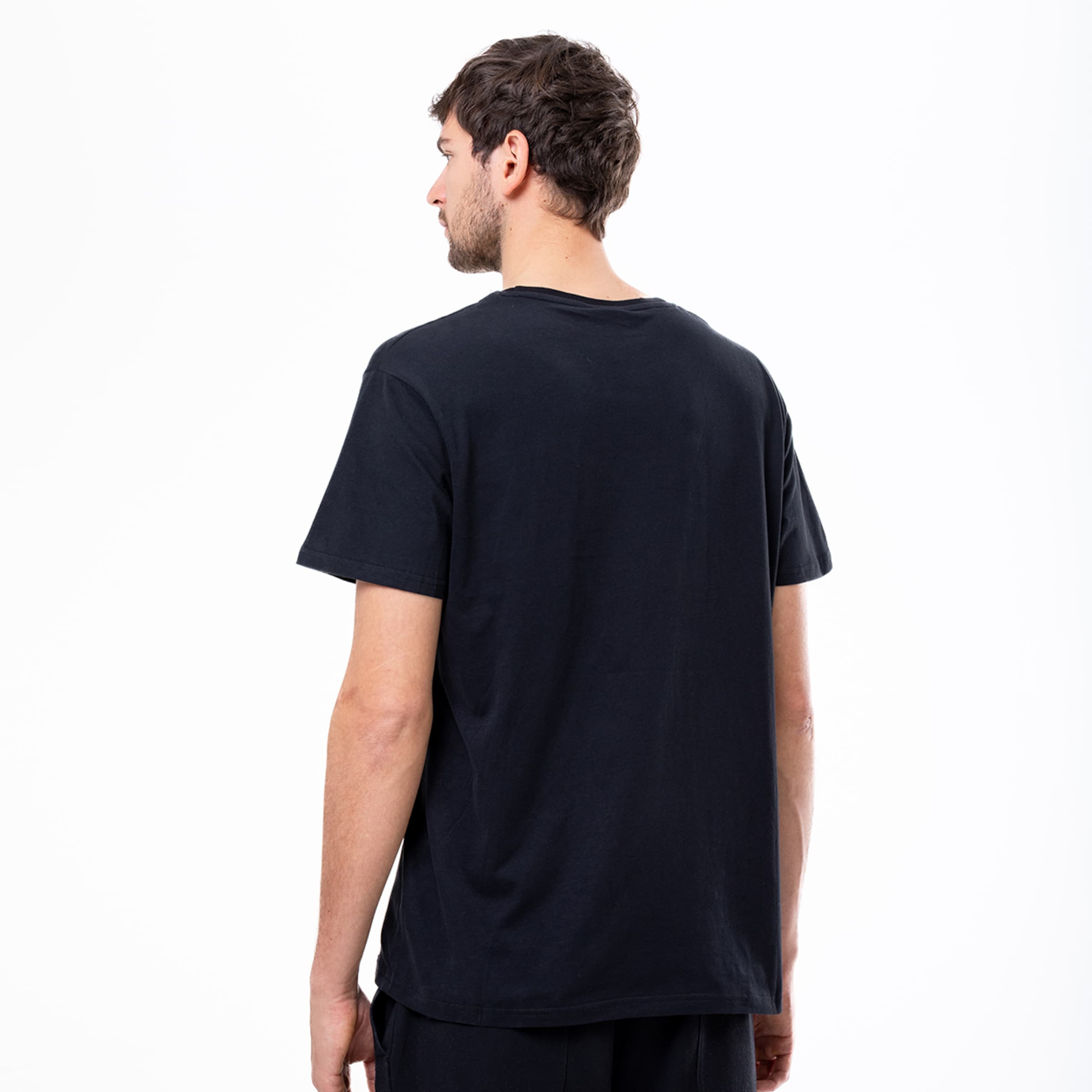 Back view of a man wearing a plain black t-shirt and black shorts against a white background.
