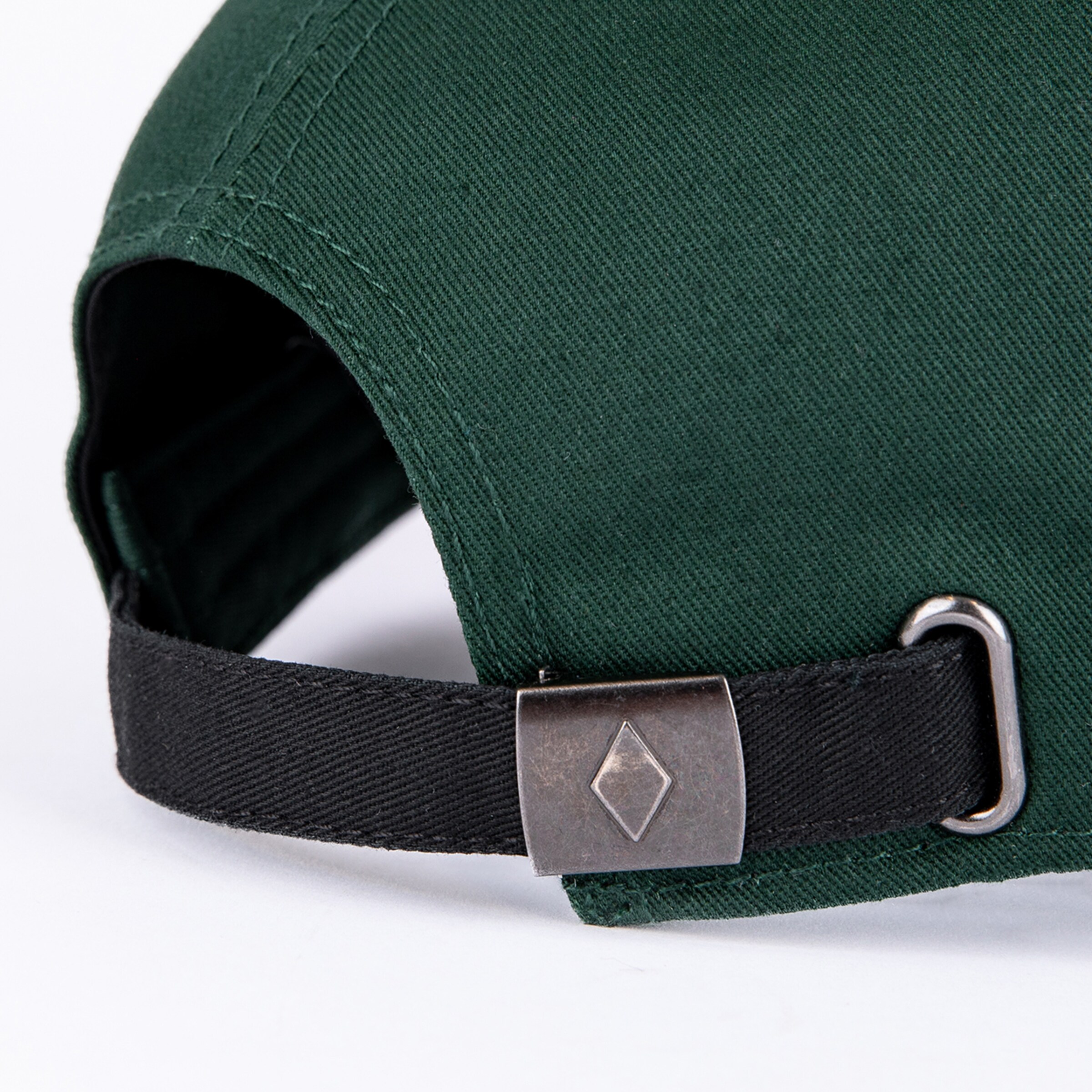 Close-up of the back of a dark green cap with an adjustable black fabric strap and a metal buckle featuring a diamond logo.