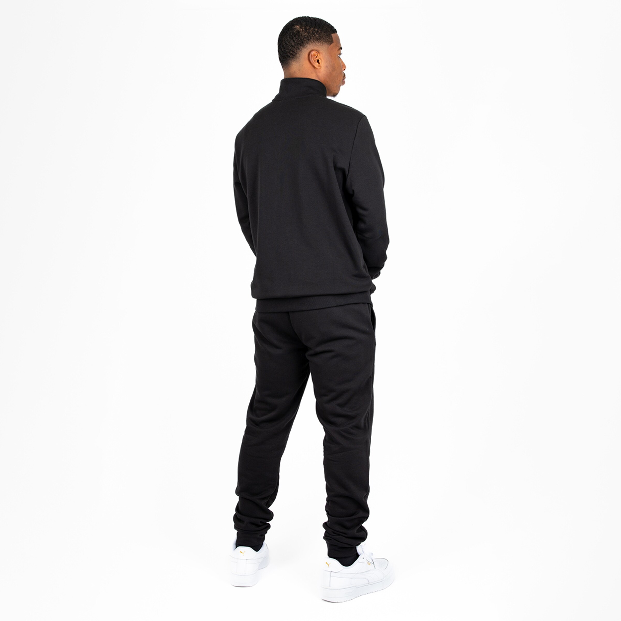 Man in a black tracksuit standing with his back to the camera.