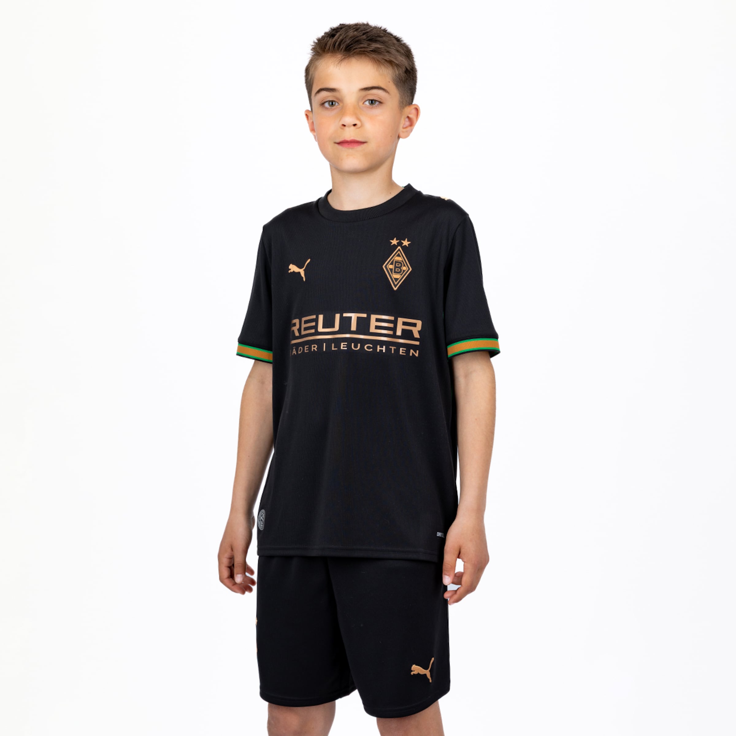 Ein Junge im schwarzen Borussia Mönchengladbach Trikot von Puma mit goldenen Logos auf weißem Hintergrund.