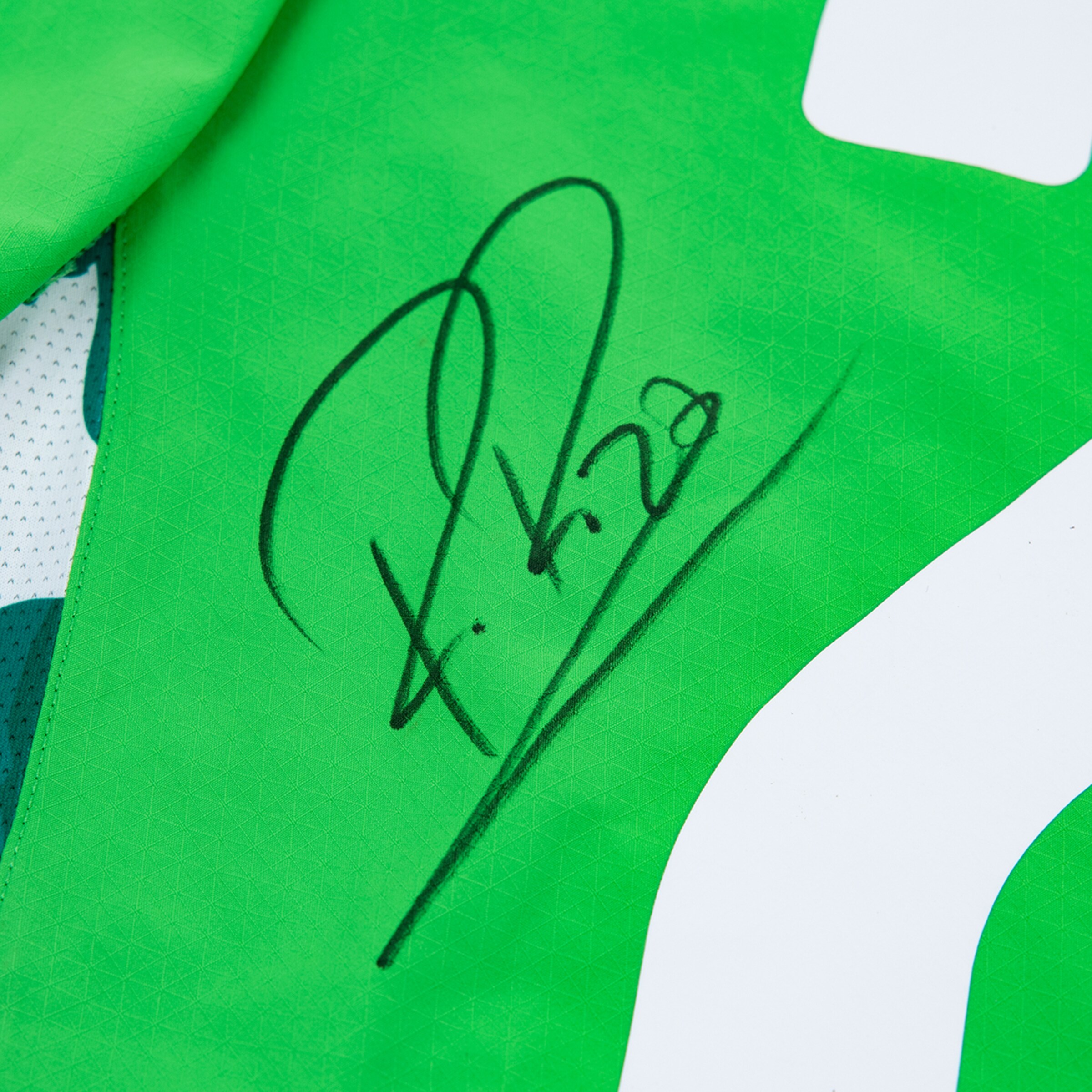 Close-up of a black signature on a bright green jersey with a partial white number visible.