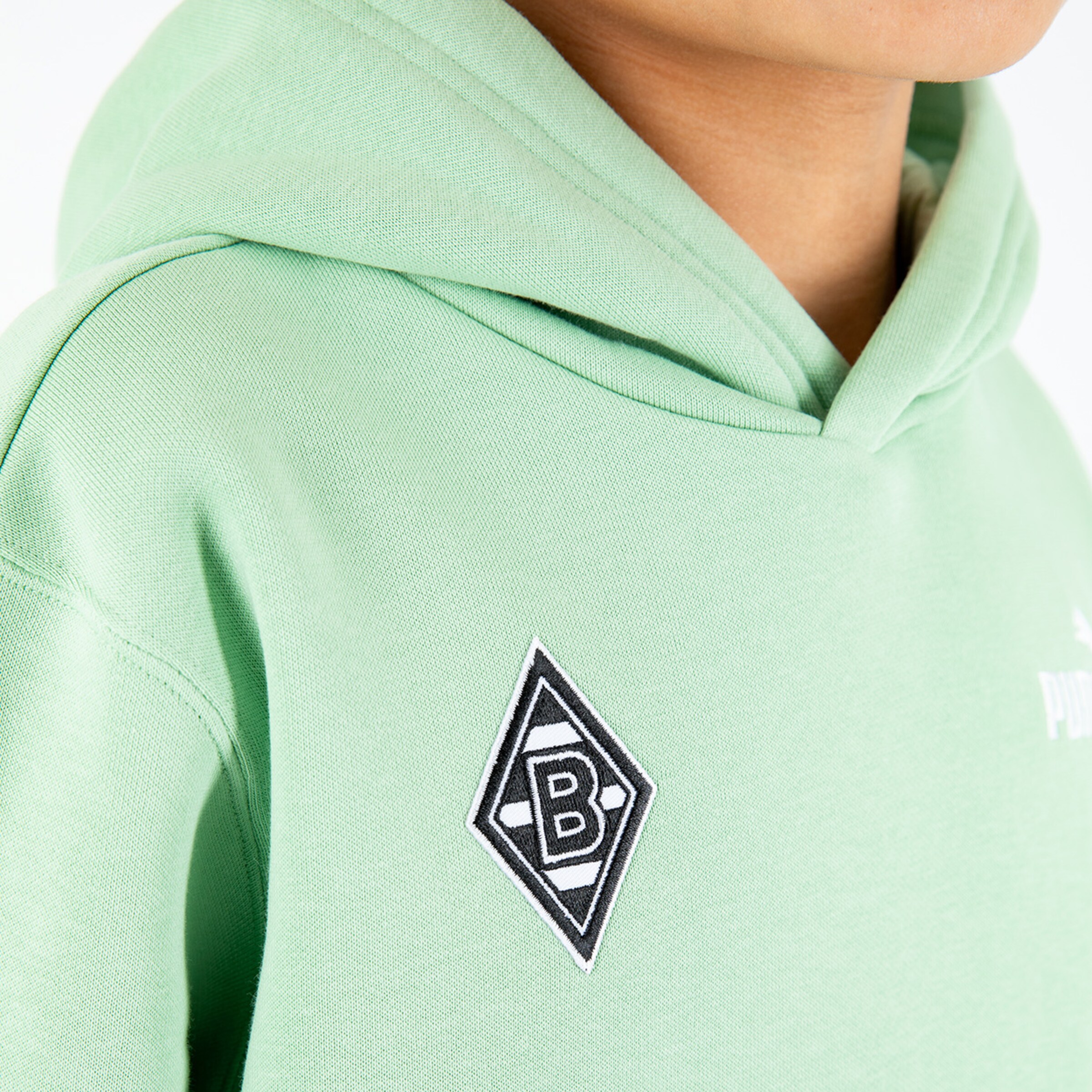 Junge trägt einen grünen Kapuzenpullover mit gesticktem Borussia Mönchengladbach-Logo.