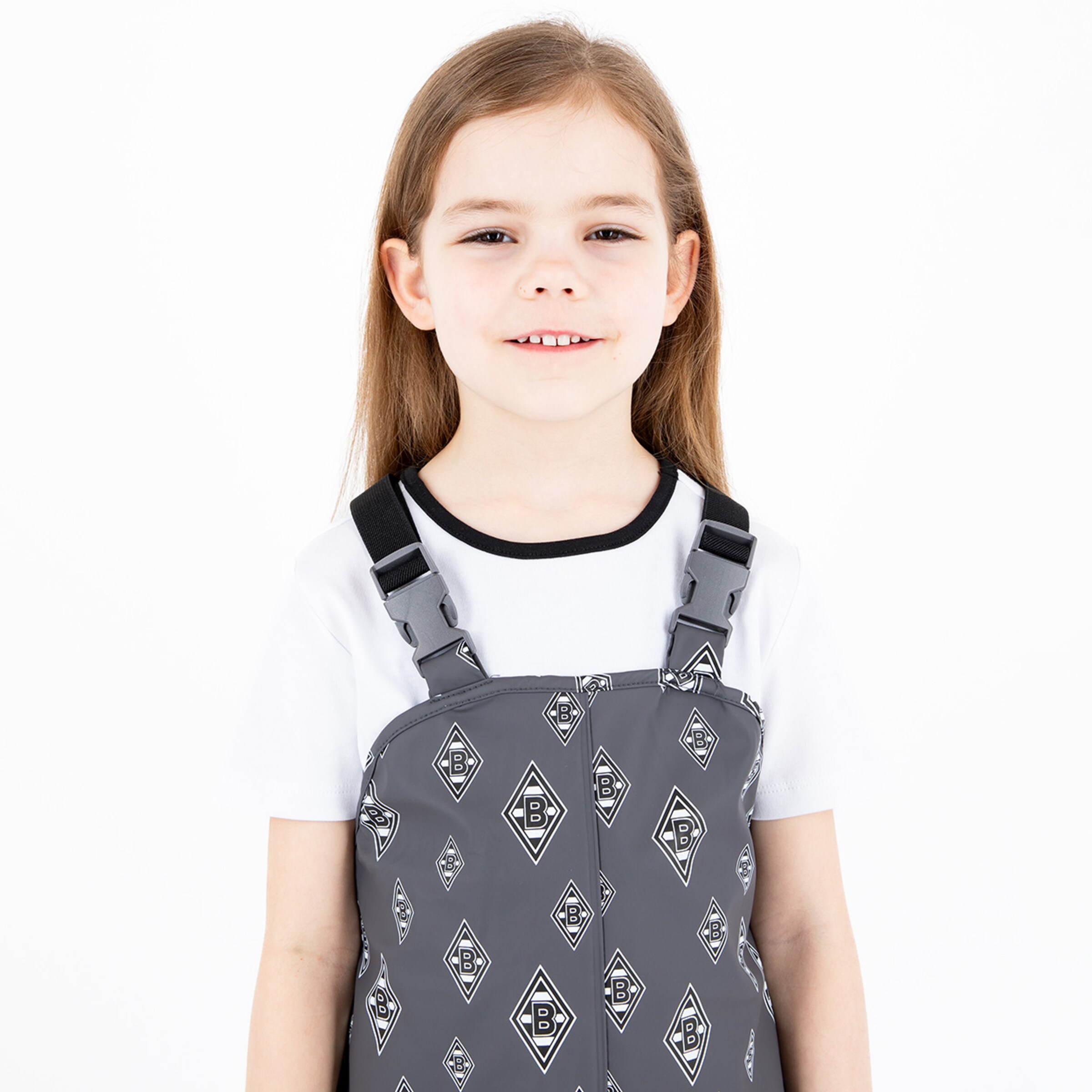 Ein kleines Mädchen trägt eine graue Latzhose mit einem Muster das das Logo von Borussia Mönchengladbach zeigt.