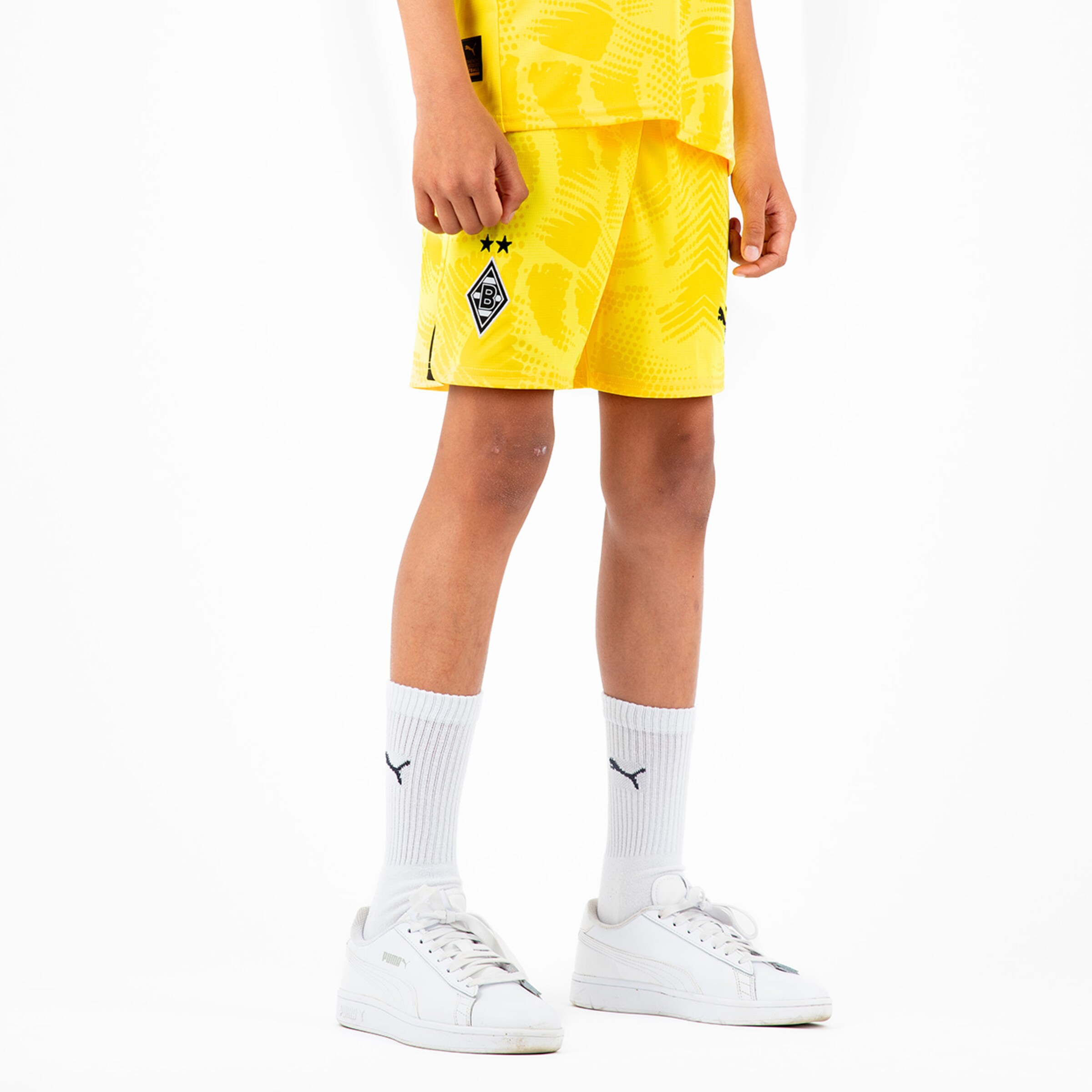 Ein Kind trägt gelbe Fußballshorts mit Borussia Mönchengladbach-Logo und weißen Socken.