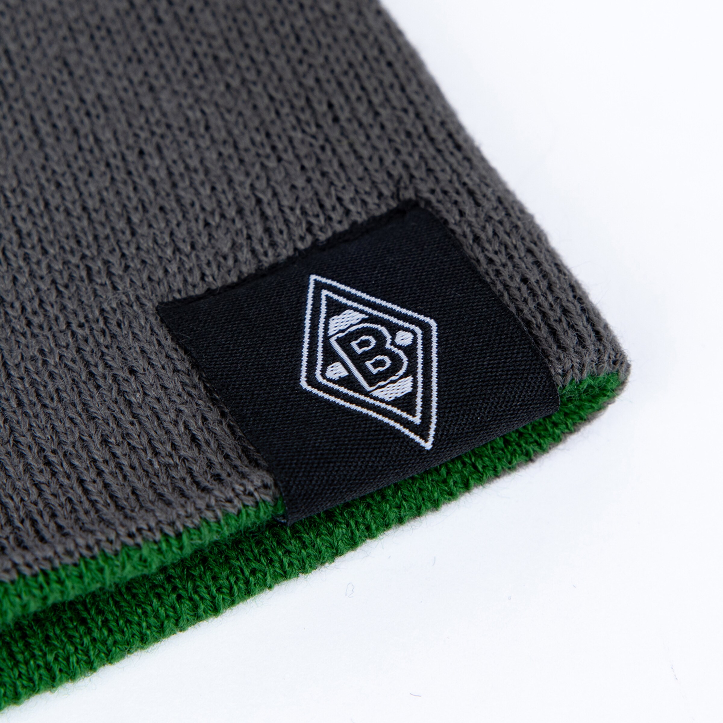 Nahaufnahme von grauem und grünem Strickstoff mit schwarzem Label und der weißen Borussia Mönchengladbach Raute.