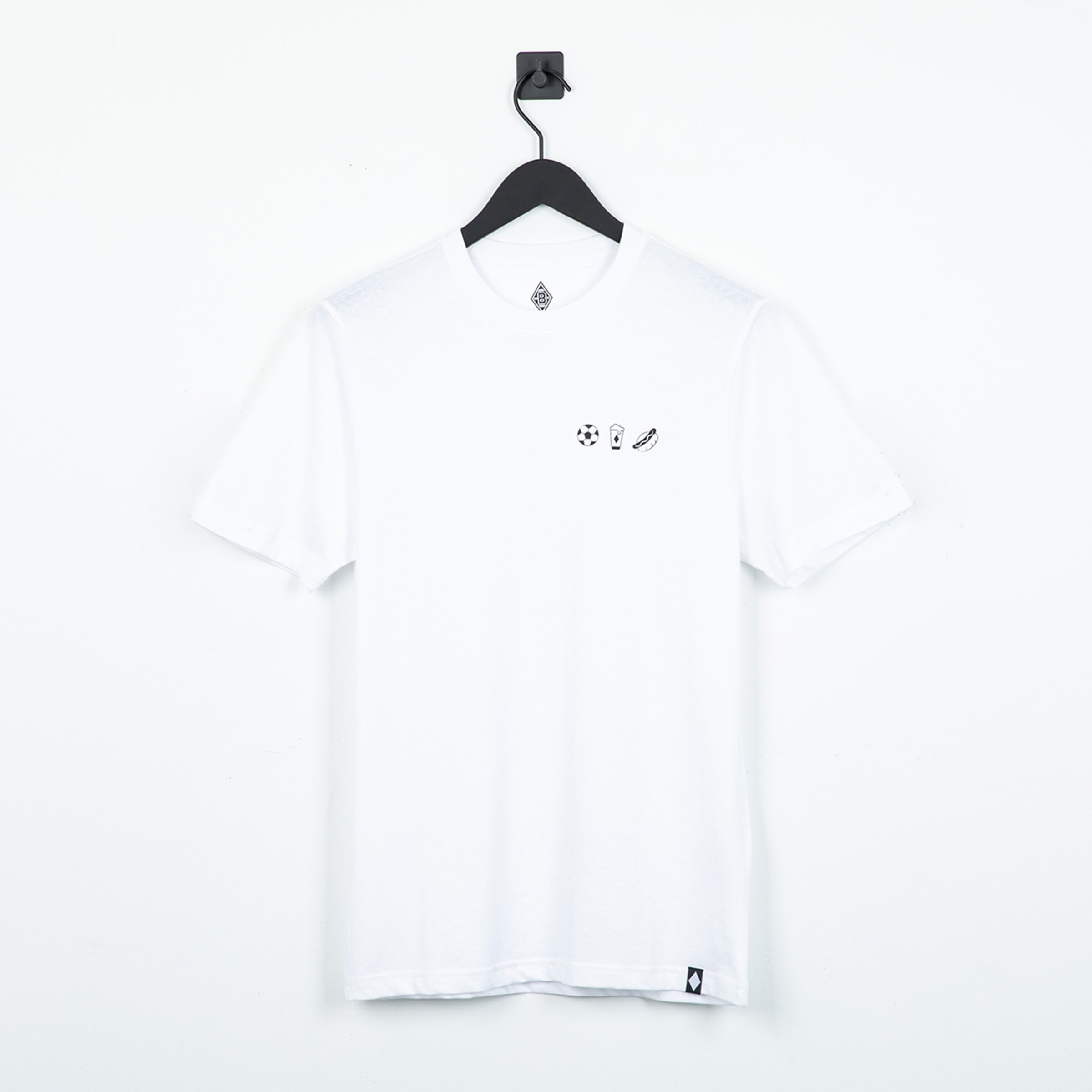Weißes T-Shirt mit kleinen Symbolen für Fußball, Bier und Hotdog auf der Brust, hängend an einem schwarzen Kleiderbügel.