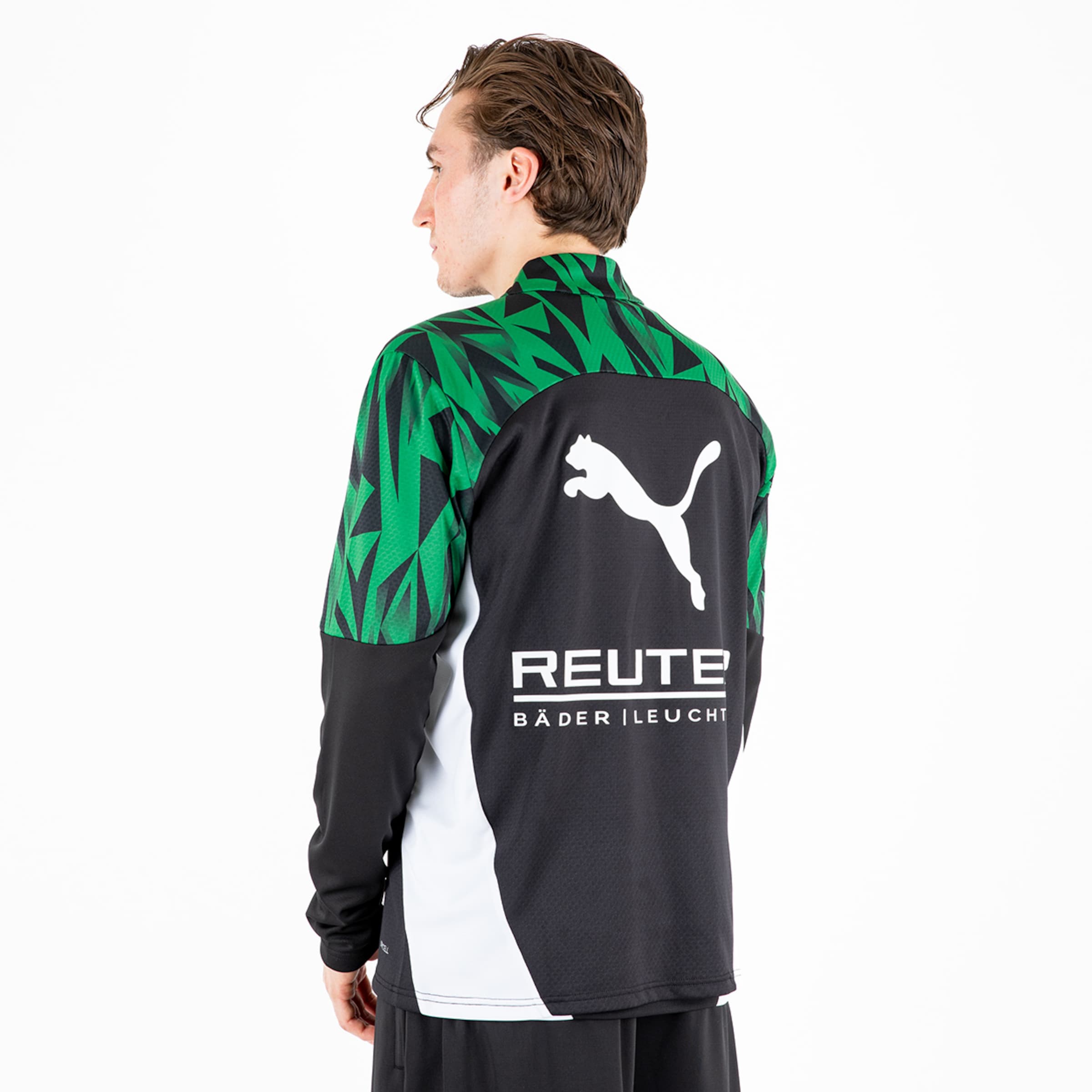 Man wearing a black and green sports jacket with a Puma logo and advertising on the back.