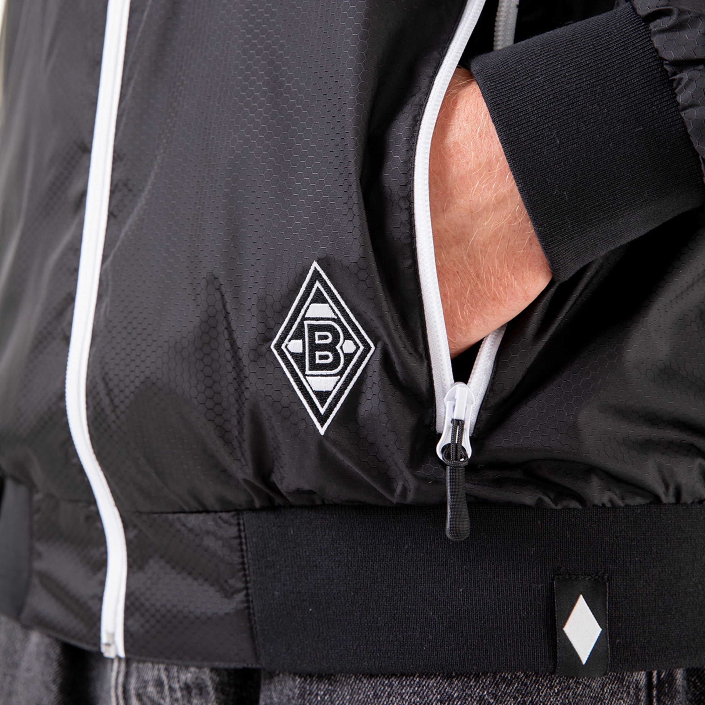 Schwarz-weiße Trainingsjacke mit Borussia Mönchengladbach-Logo auf der Brust.