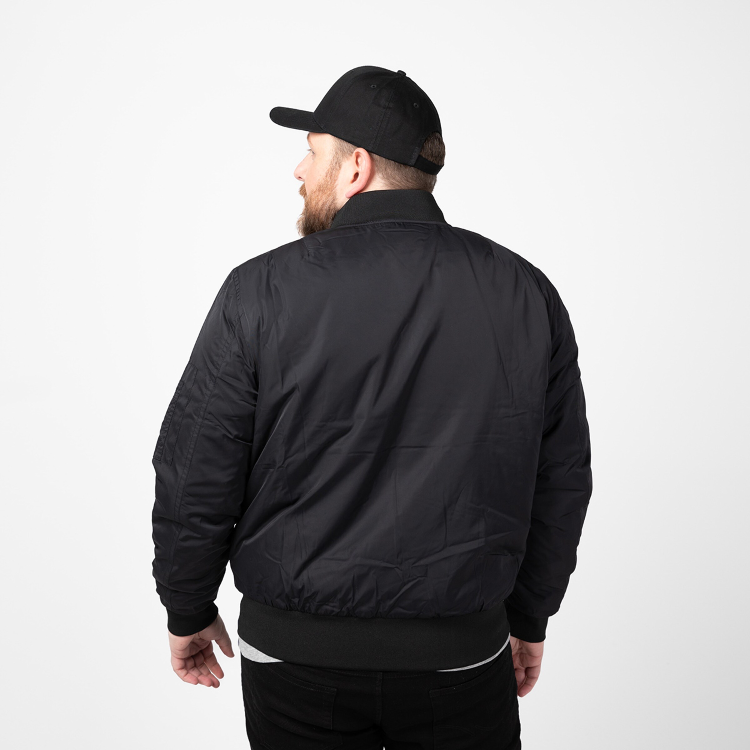 Man wearing a black bomber jacket and black cap seen from behind.