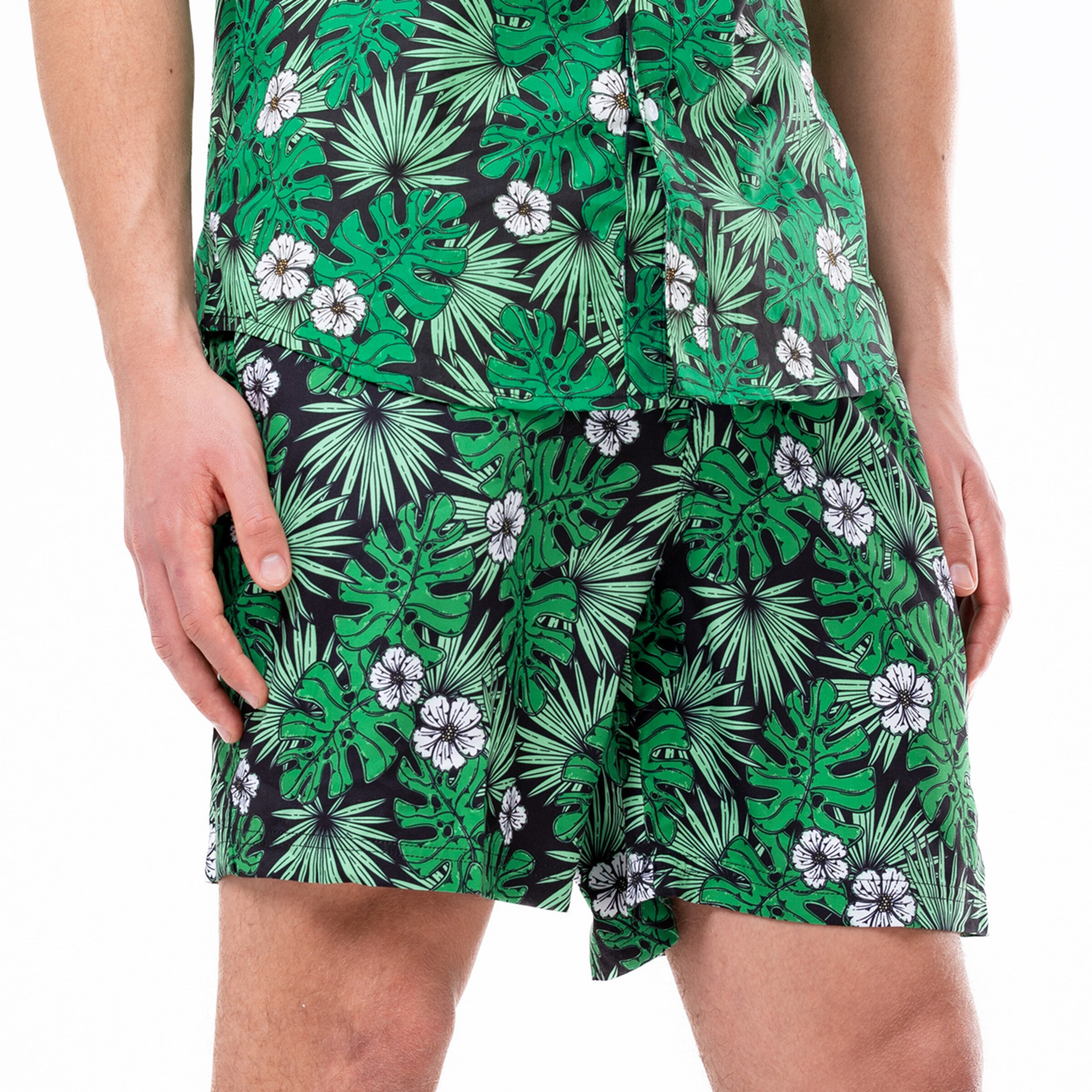 Ein Mann trägt ein kurzärmliges Hemd und Shorts mit einem tropischen Blattmuster.