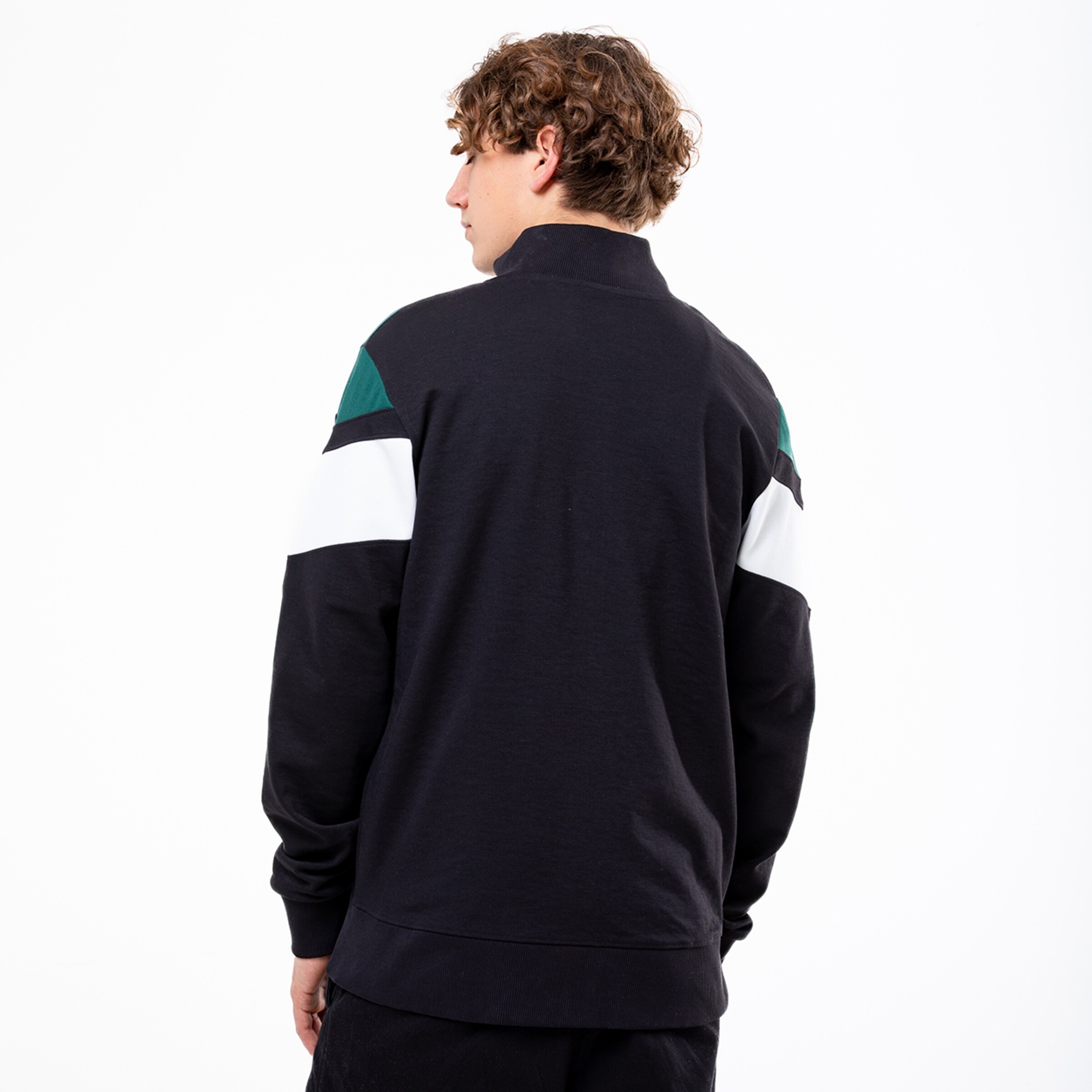 Mann mit lockigem blondem Haar trägt einen schwarzen Sweatshirt mit mehrfarbigen Ärmeln von hinten.