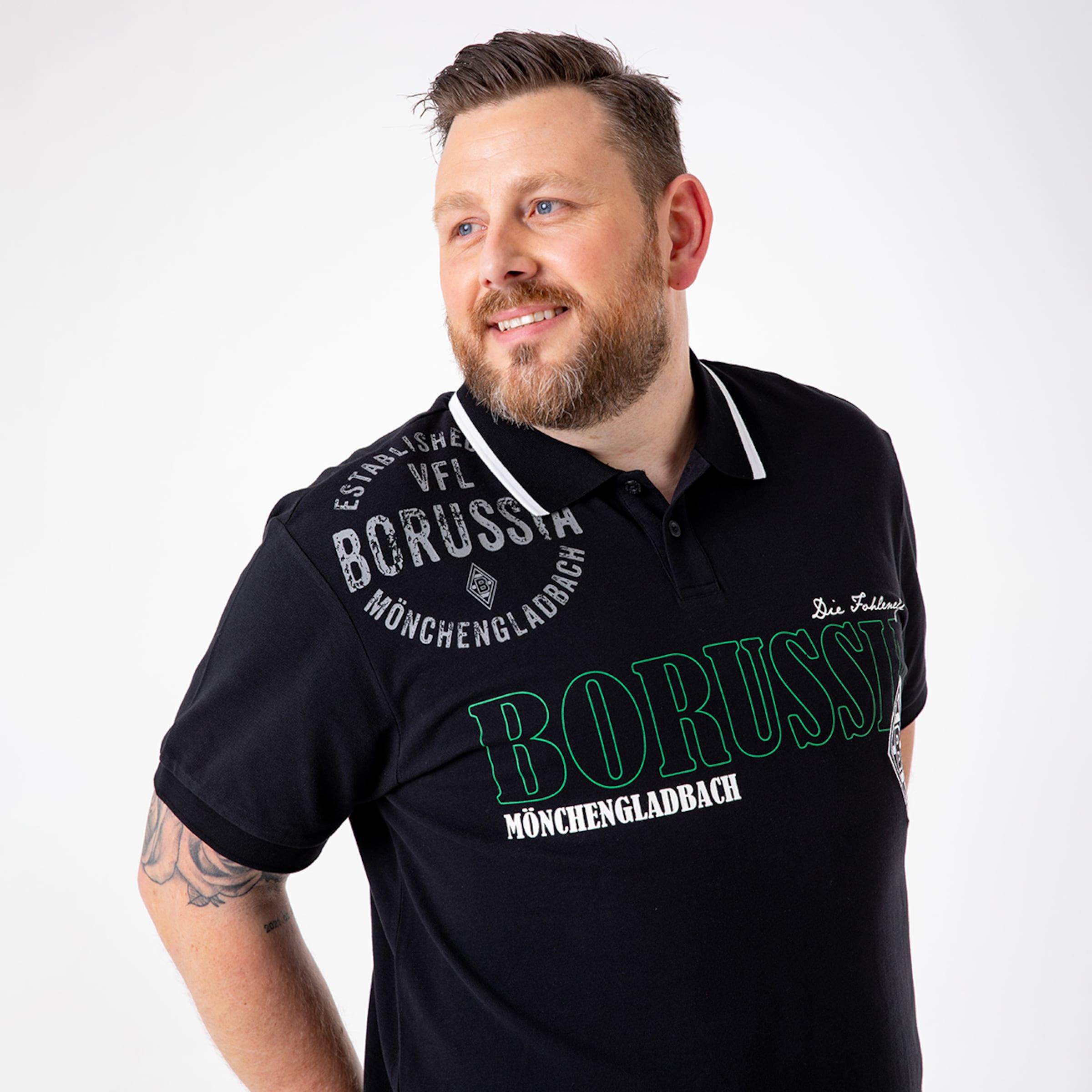 Man with short hair wearing a black polo shirt featuring Borussia Mönchengladbach print.