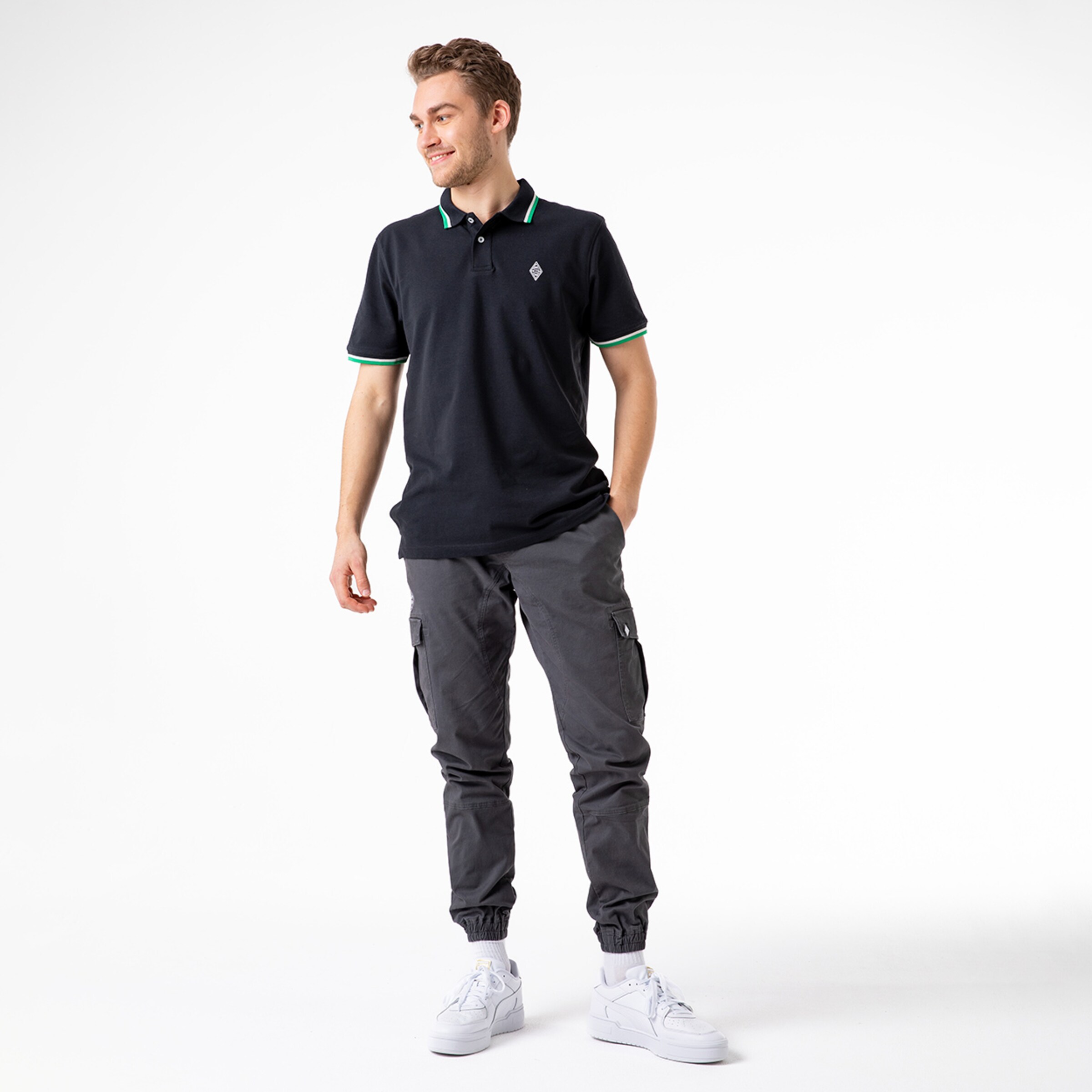 Young man wearing a black polo shirt with green collar gray cargo pants and white sneakers.