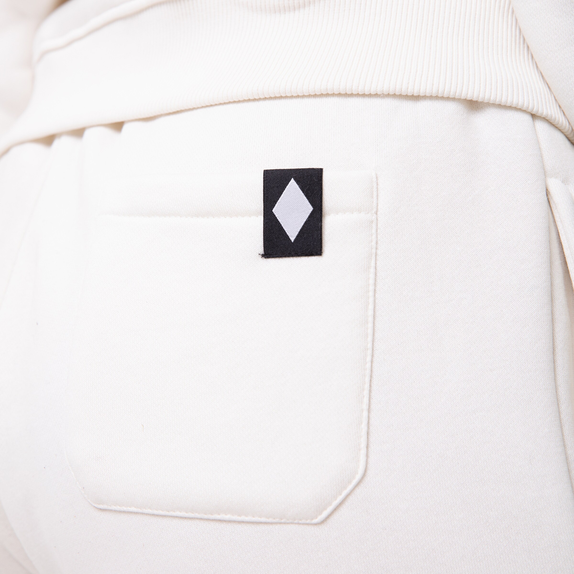 Helle Hose mit einer kleinen schwarzen Aufnähere im Gesäßbereich.