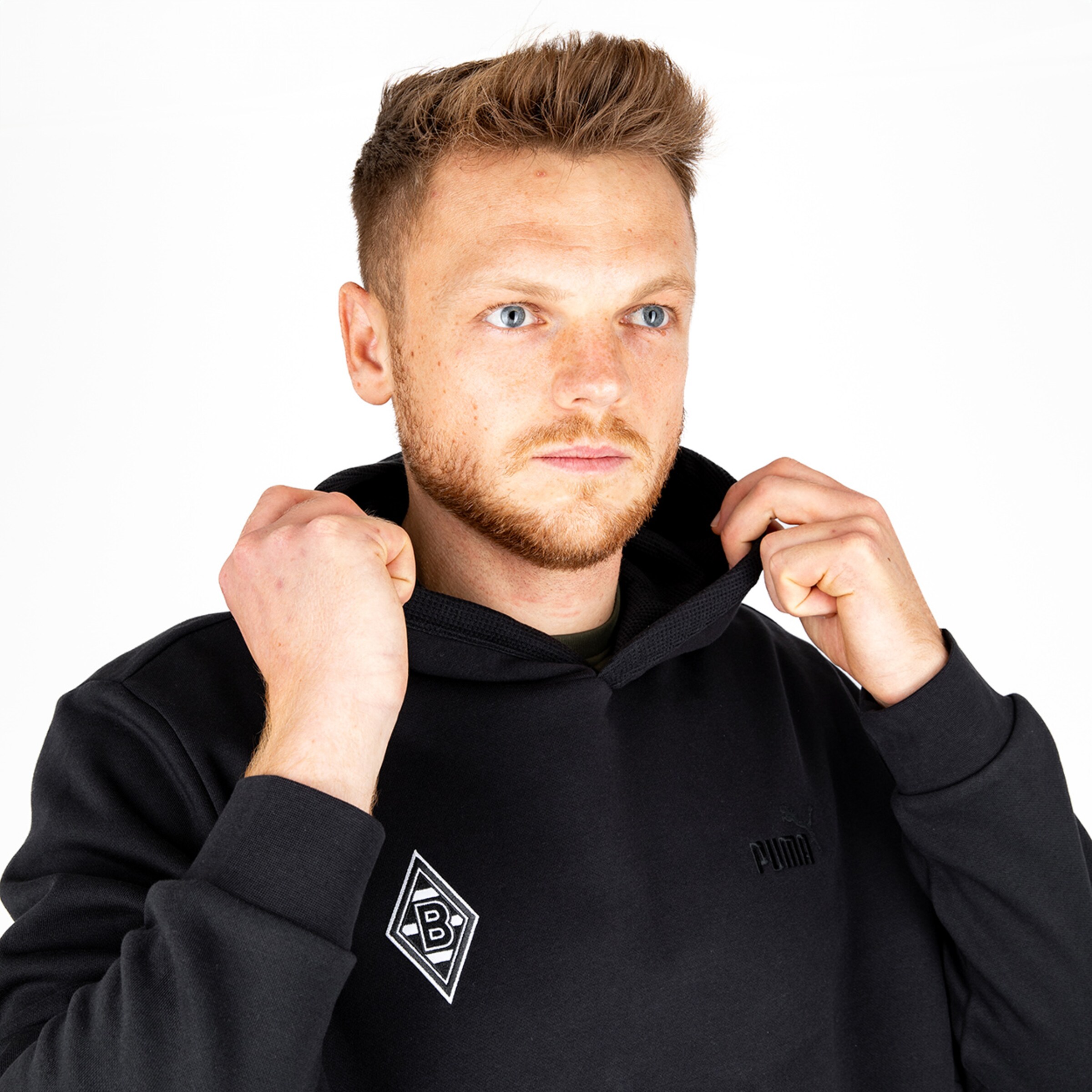 Junger Mann mit kurzem blondem Haar trägt einen schwarzen Hoodie mit einem Aufnäher von Borussia Mönchengladbach.