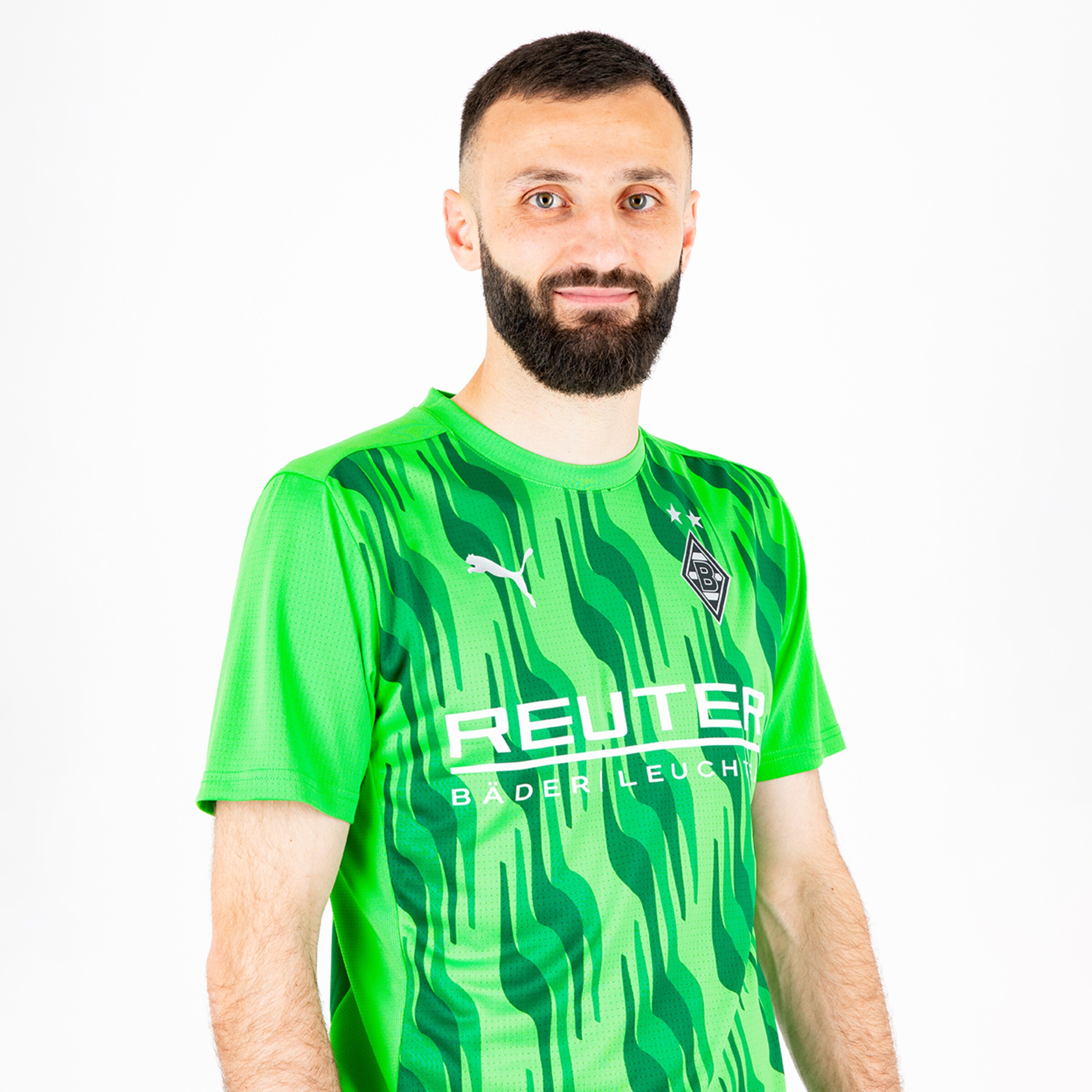 Ein Spieler trägt ein grünes Trikot mit Wellenmuster und steht vor neutralem Hintergrund.