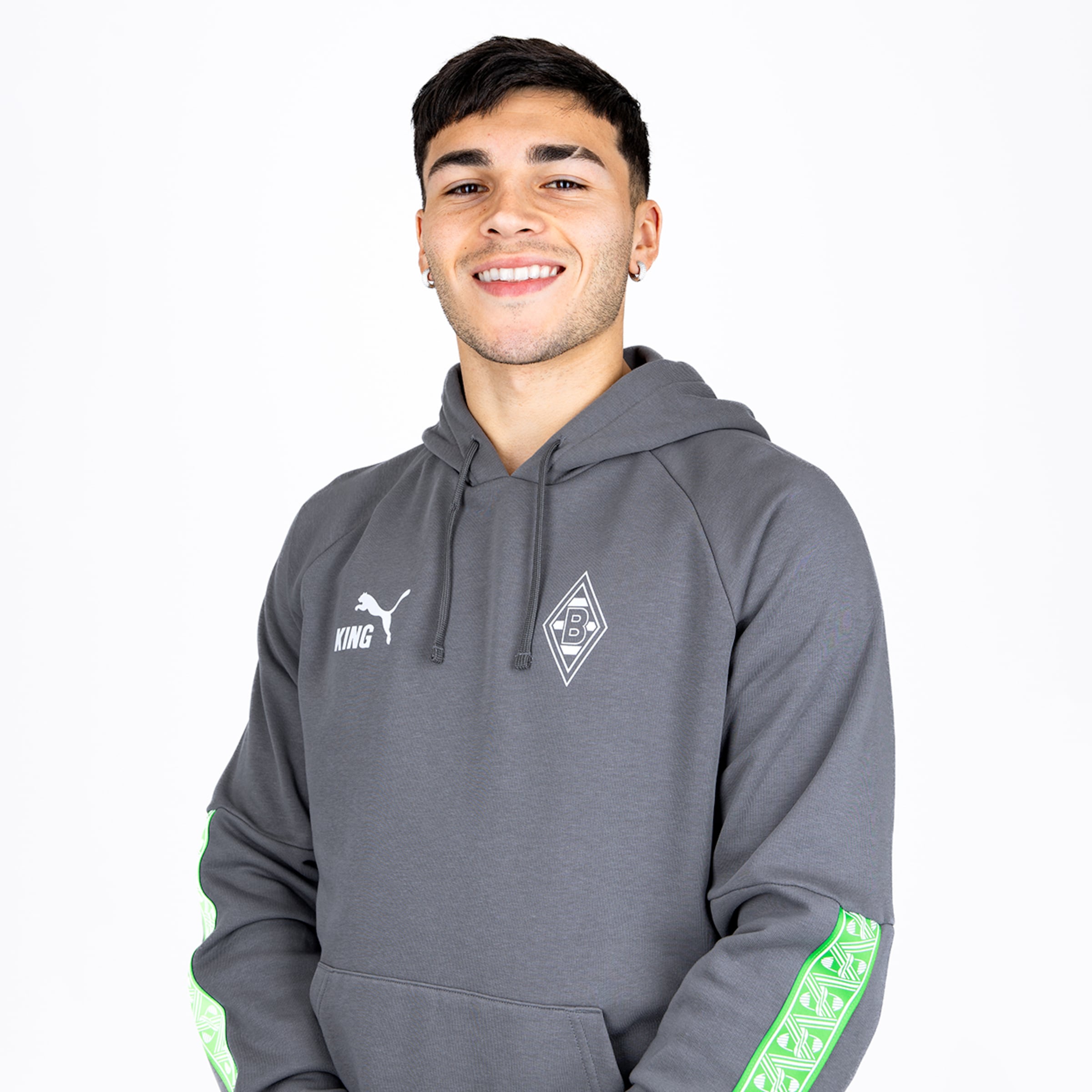 Smiling young man in a grey Puma hoodie with the Borussia Mönchengladbach logo against a white background.
