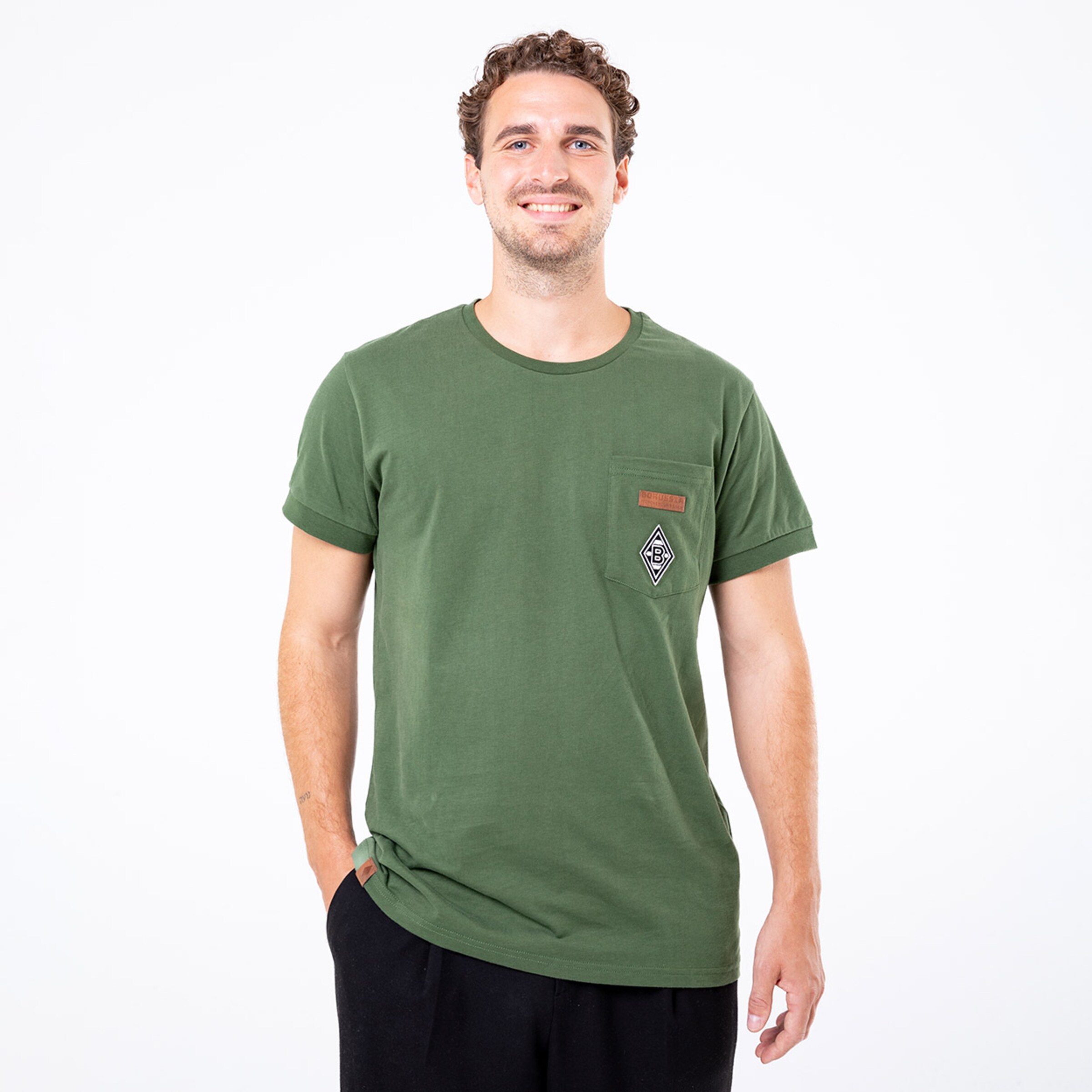 Mann trägt ein grünes T-Shirt mit einer Brusttasche und einem quadratischen Aufnäher.