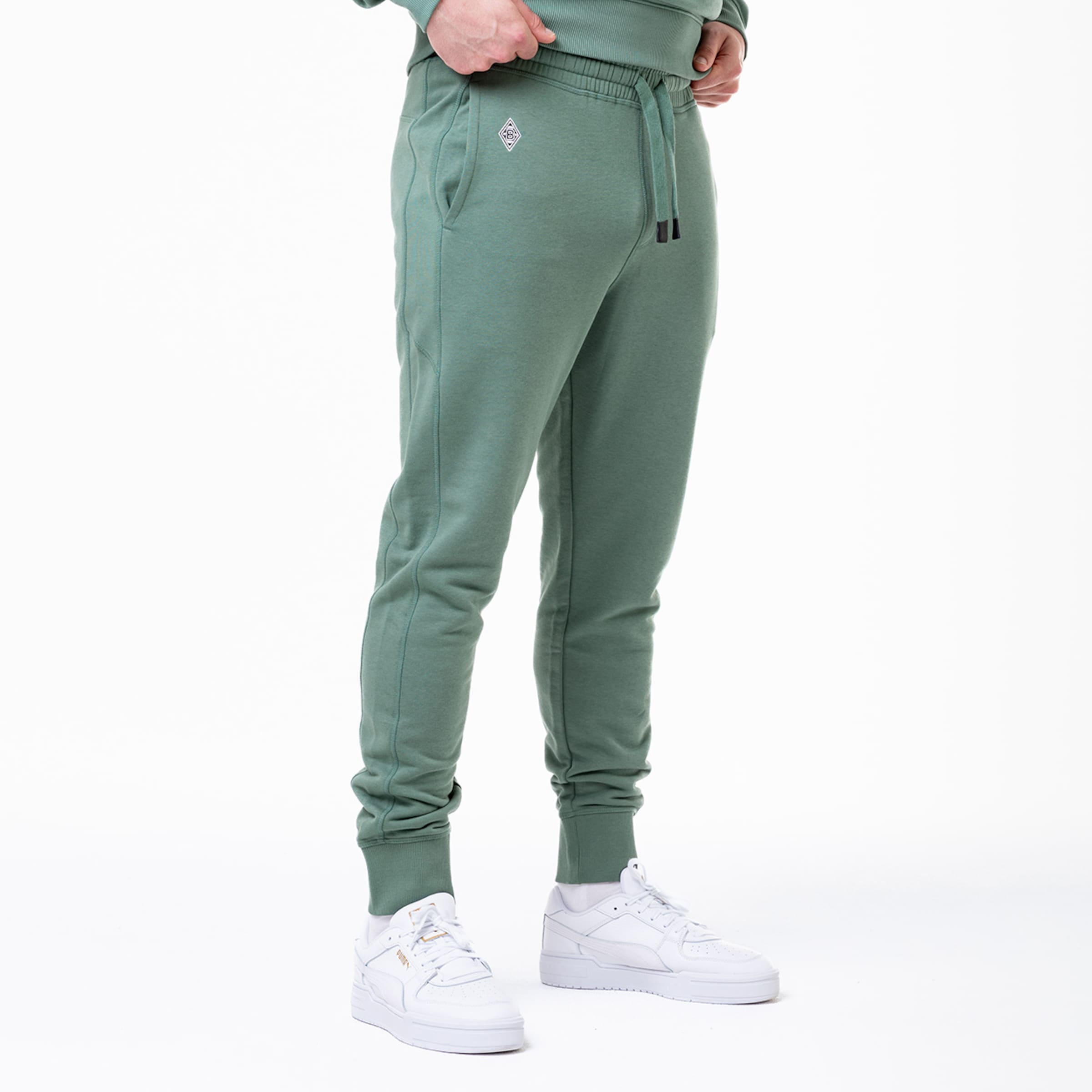 Grüne Jogginghose mit elastischem Bund und logo getragen mit weißen Sneakers.