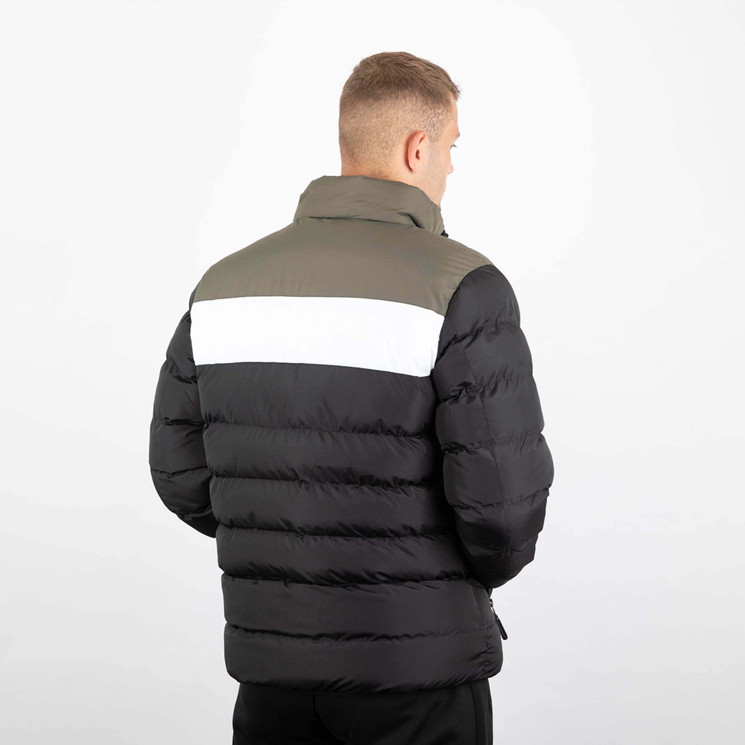 Eine Person von hinten in einer gesteppten Jacke mit grauem schwarzem und weißem Farbblockdesign.