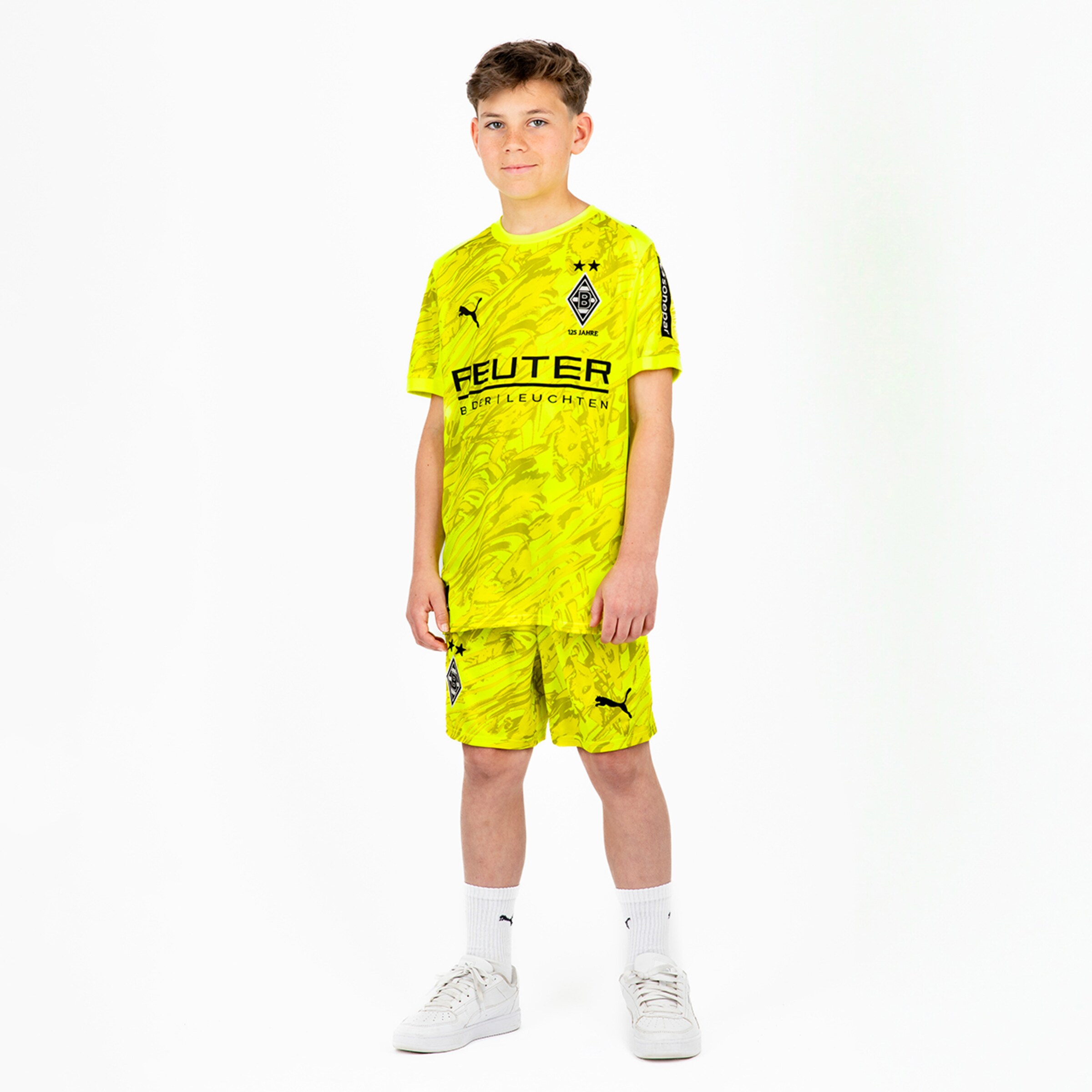 Junge in gelbem Borussia Mönchengladbach-Trikot und Shorts steht aufrecht mit neutralem Gesichtsausdruck.