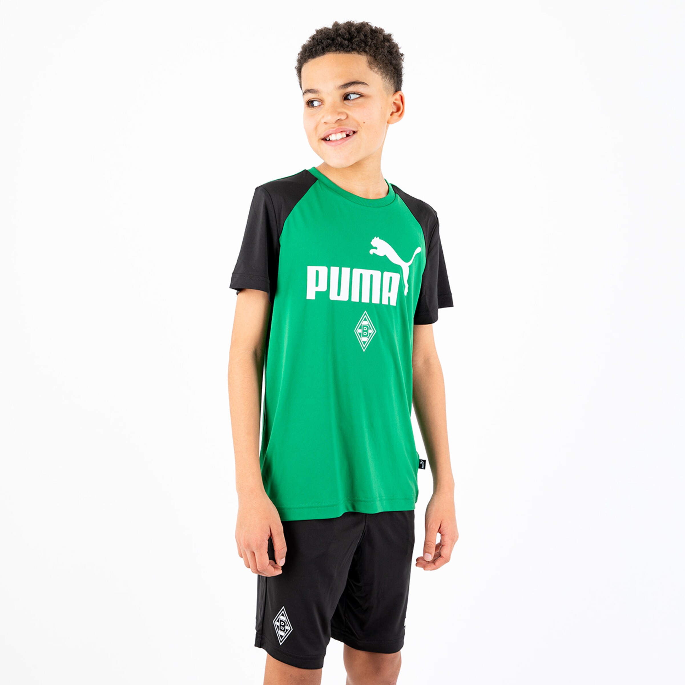 Ein Junge trägt ein grünes Puma-Trikot mit schwarzem Ärmel und schwarze Shorts.