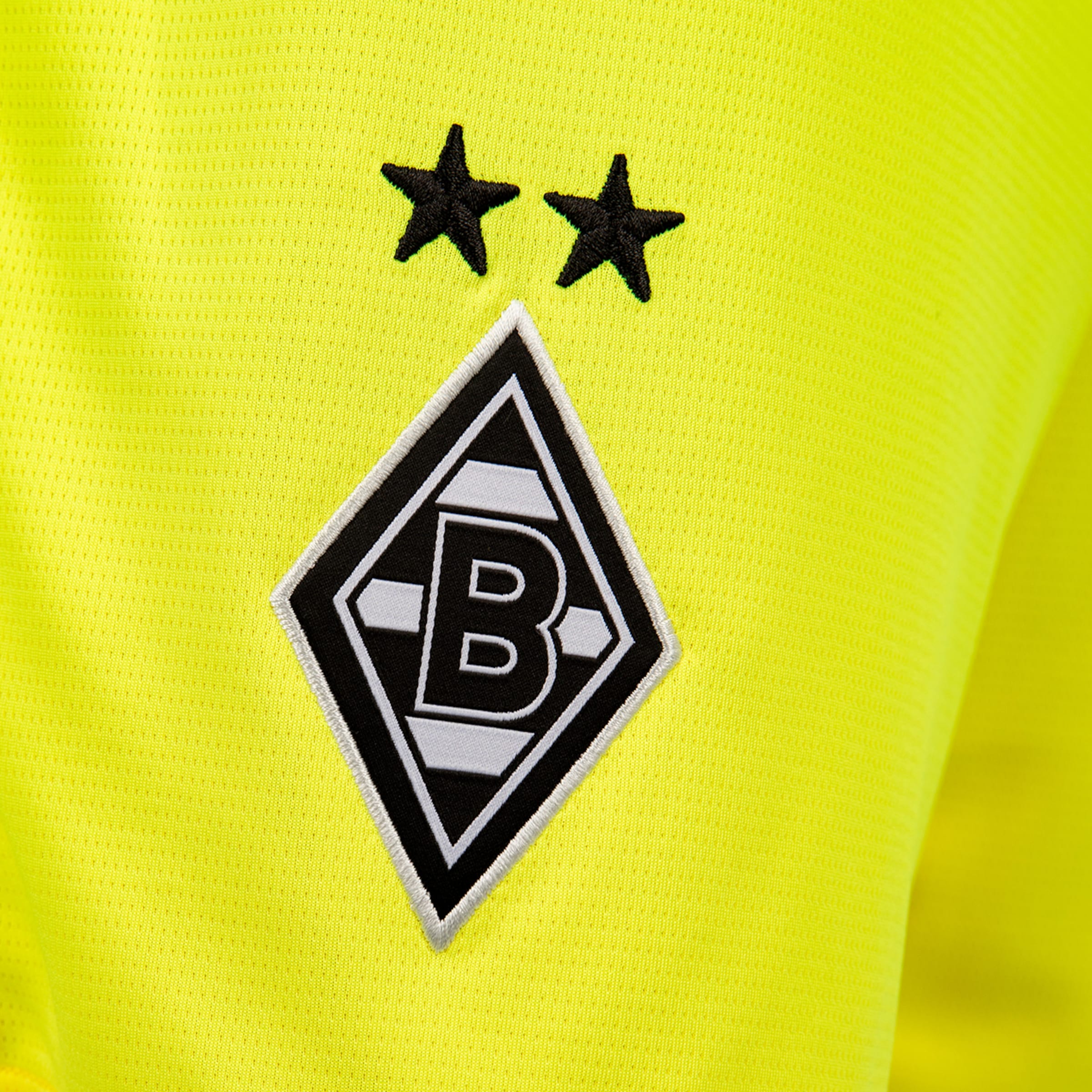 Close-up of a neon yellow jersey with the Borussia Mönchengladbach crest (diamond with a "B") and two black stars embroidered above it.