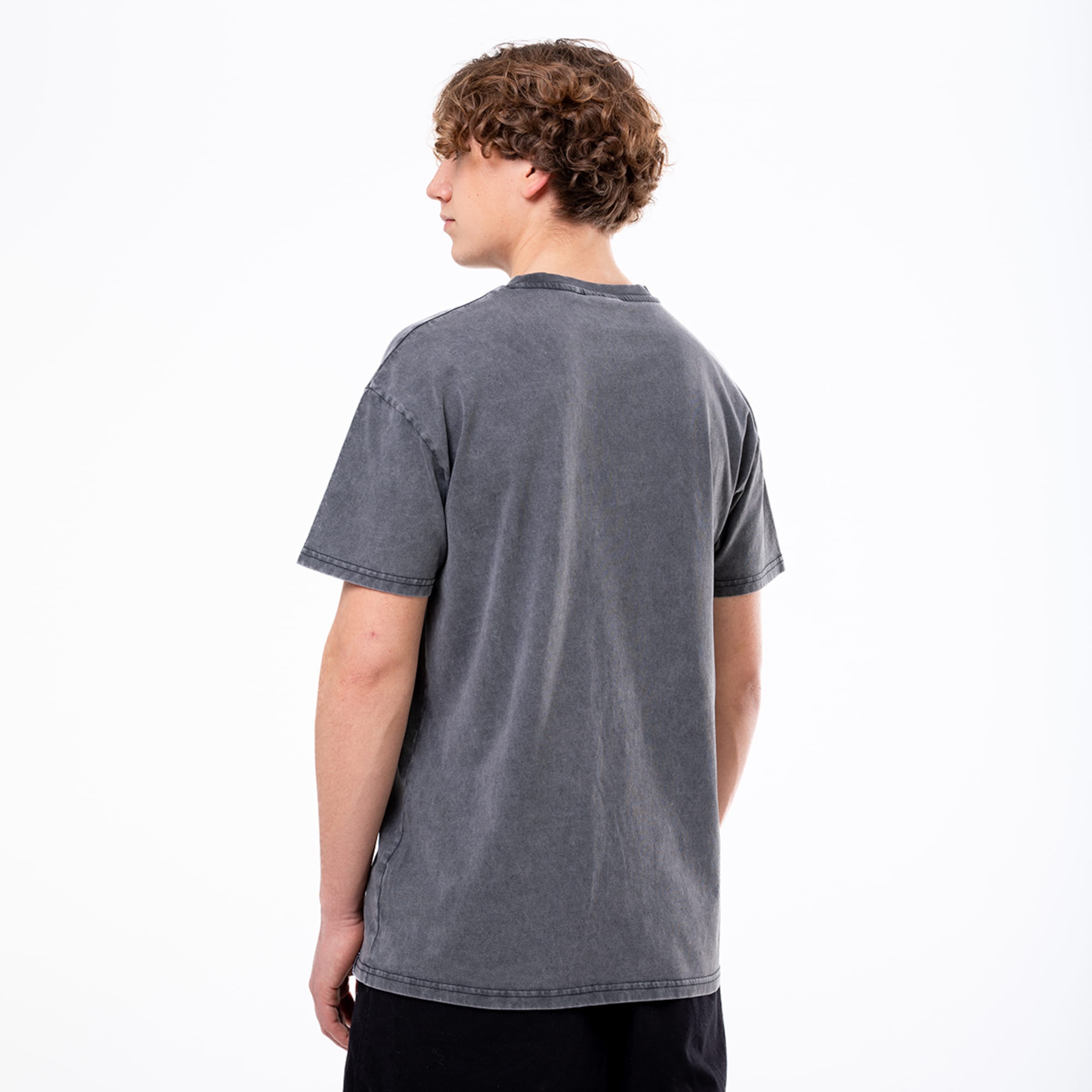 Mann mit lockigen hellbraunen Haaren trägt ein graues T-Shirt von hinten sichtbar.