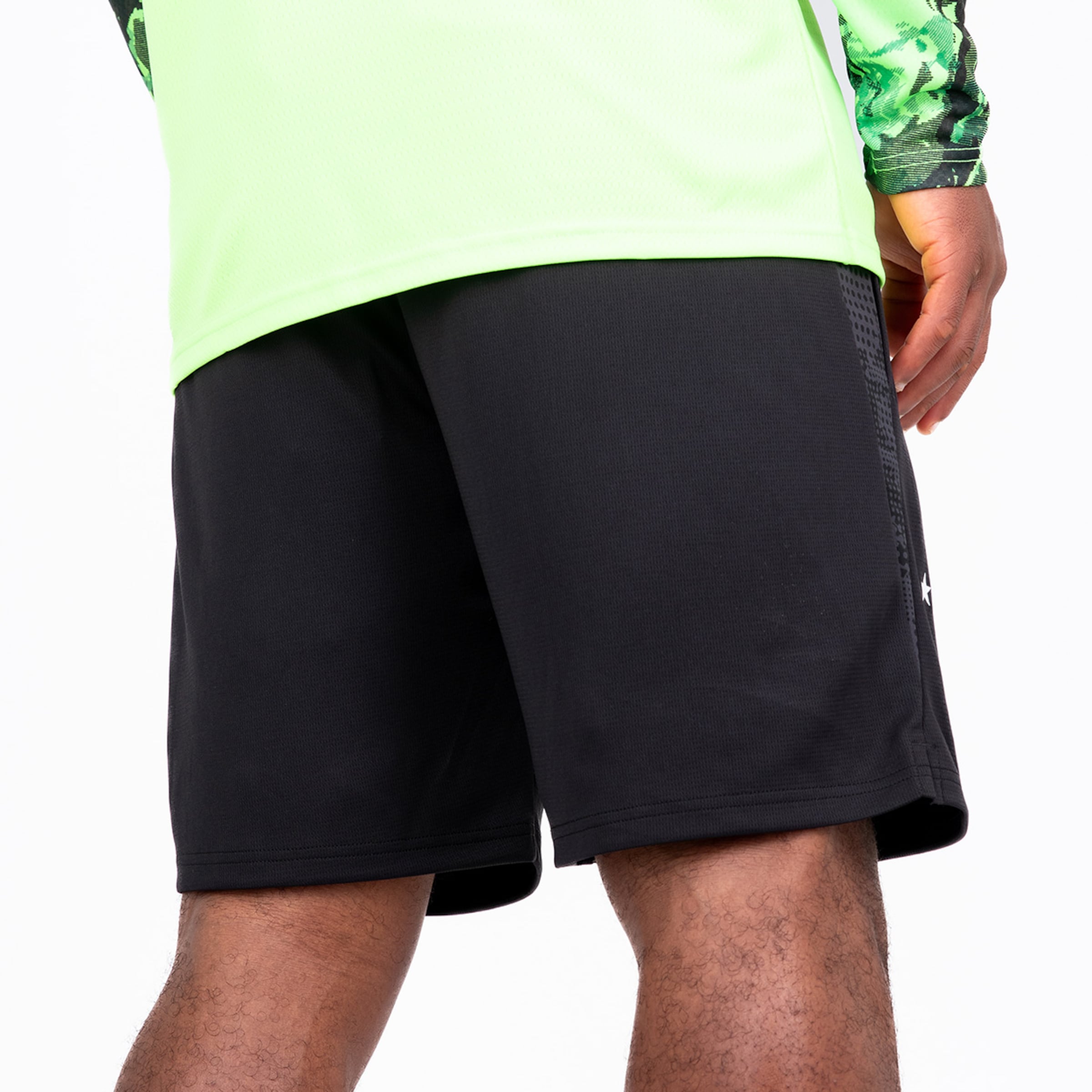 Rückansicht eines Mannes in neongrünem Langarmshirt und schwarzen Sportshorts vor weißem Hintergrund.