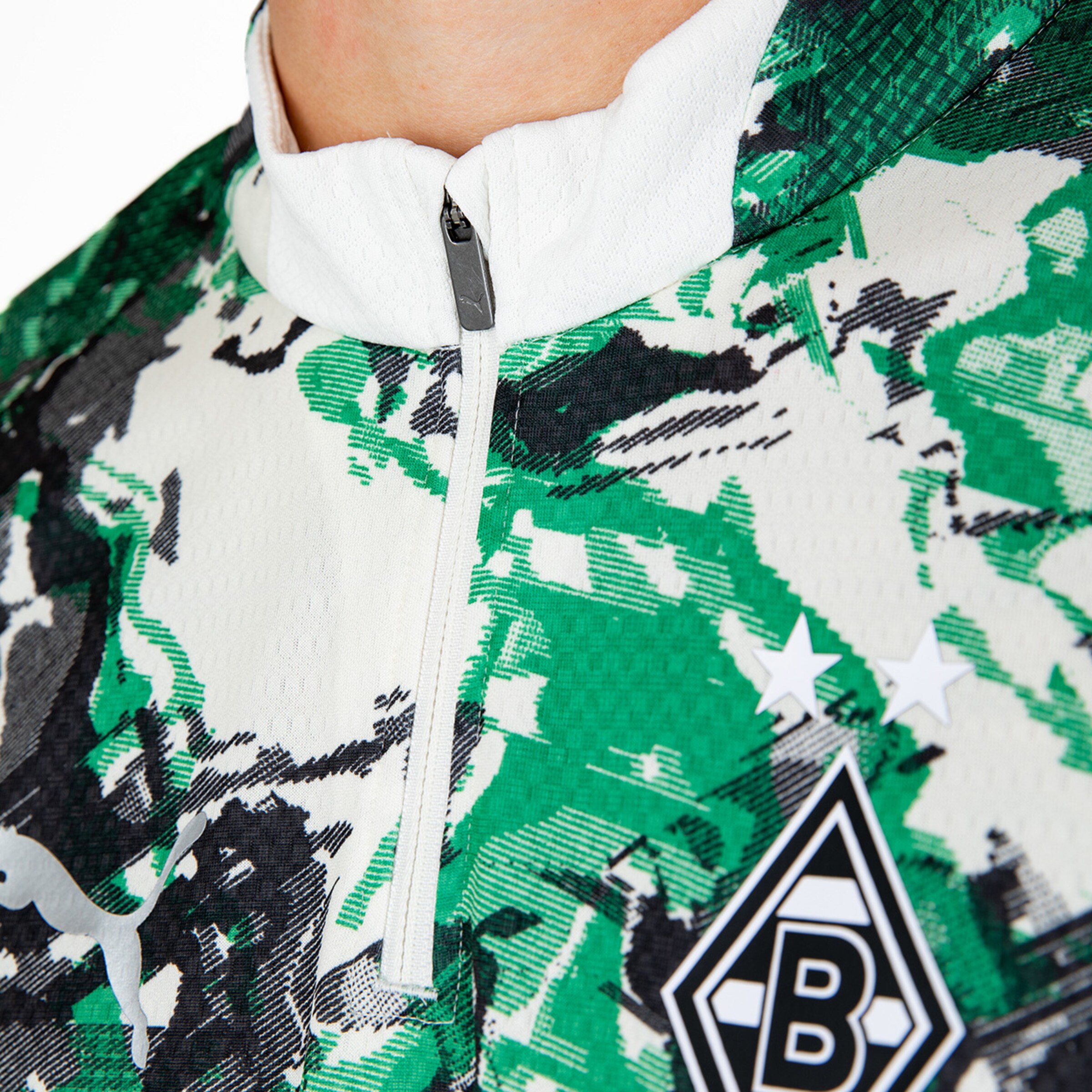 Detailaufnahme eines Sportoberteils mit grünem gemustertem Stoff und einem Reißverschluss.