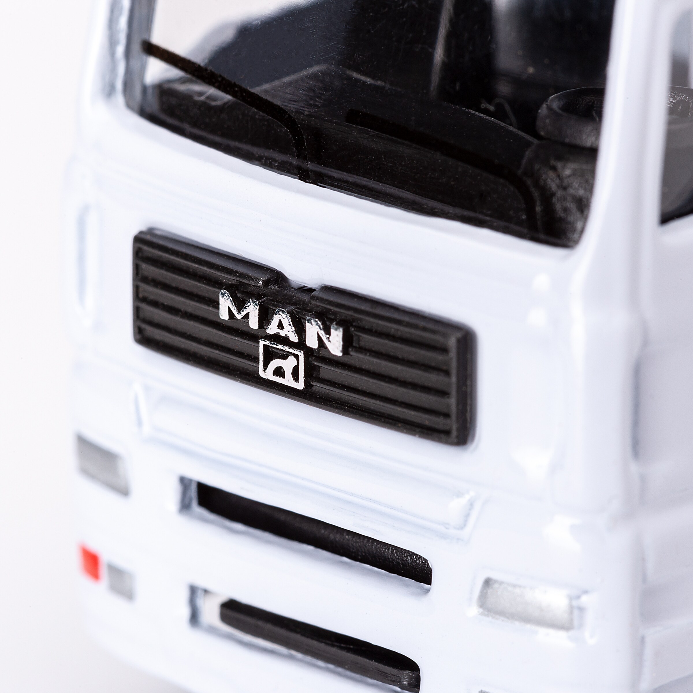Close-up of a white MAN model truck's front, showing the black grille with the MAN lettering and lion emblem.